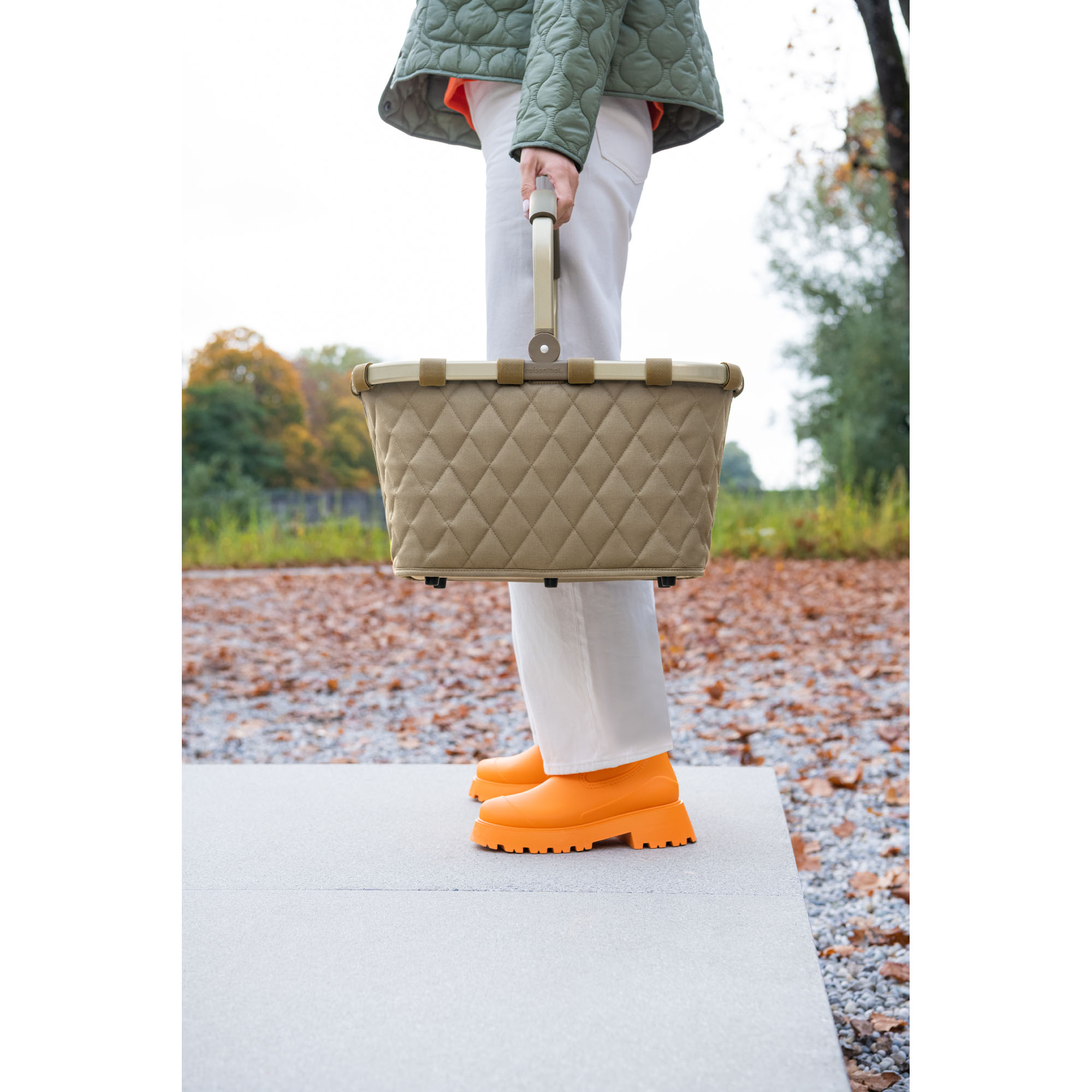 Einkaufskorb von Reisenthel, Modell Carrybag, in Olivbeige mit Rautensteppung und hellen Rahmendetails, von einer Person am Griff getragen.