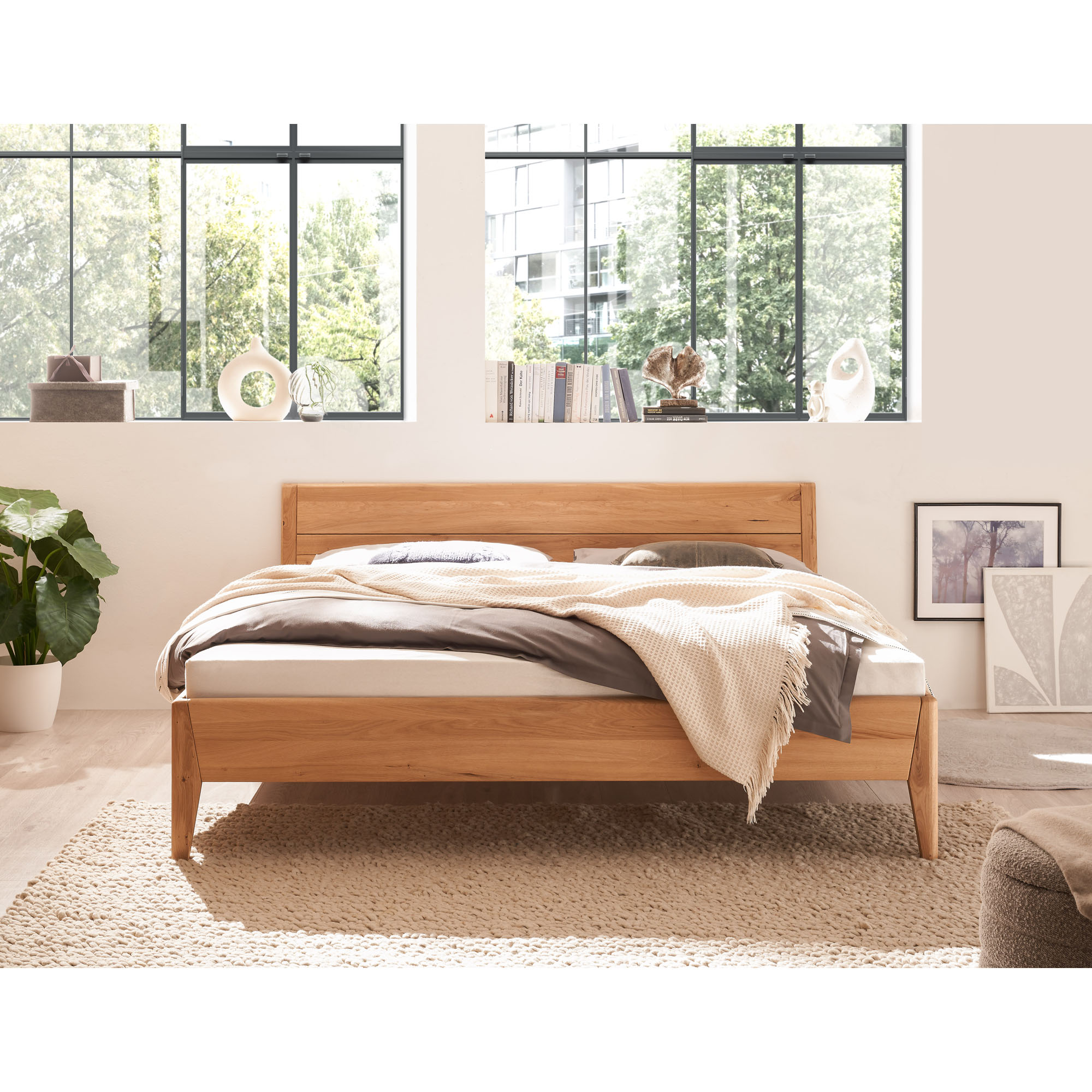Bett aus Holz mit Kopfteil in frontaler Ansicht in einem hellen Schlafzimmer