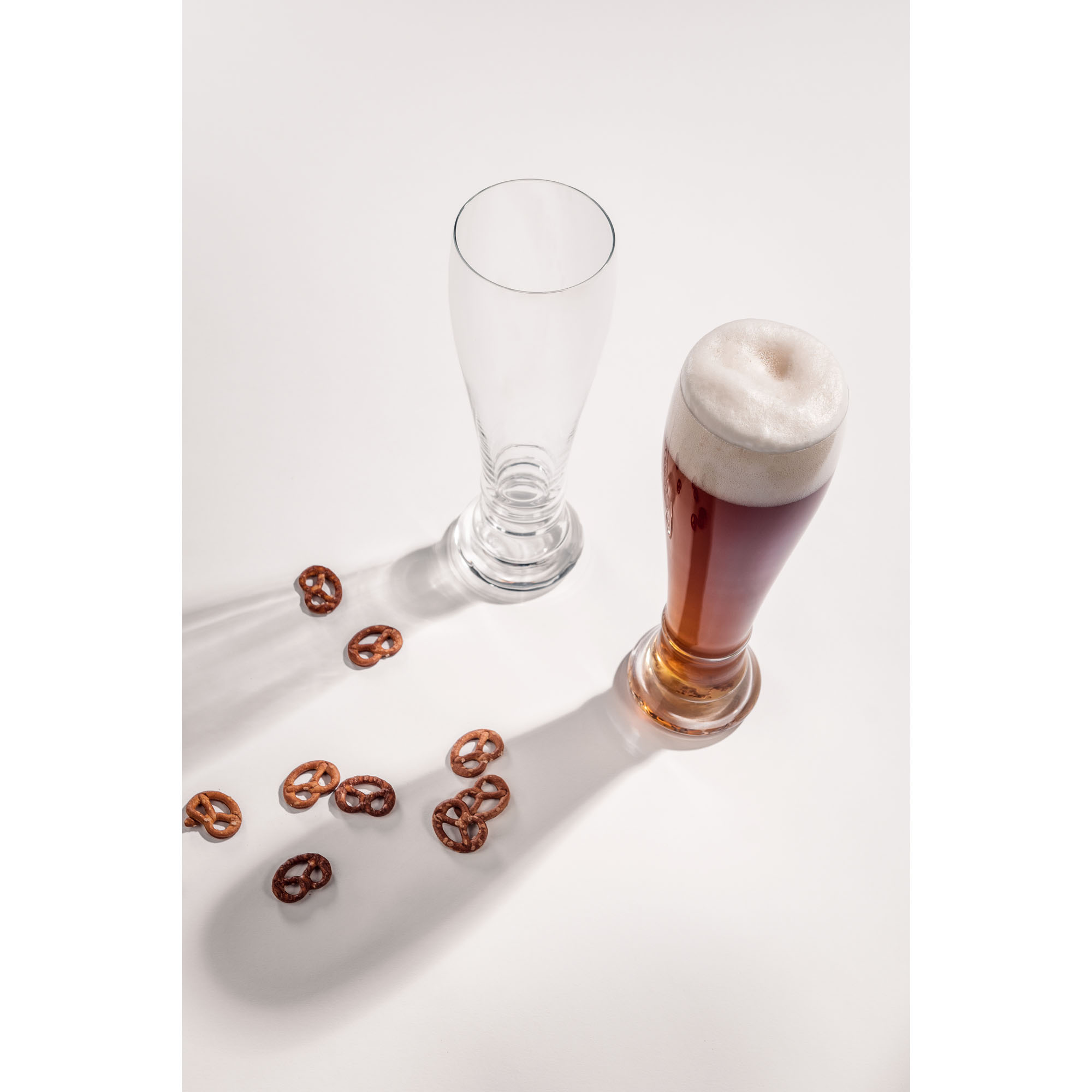 Zwei Beer-Basic-Weizenbiergläser auf heller Fläche, eines leer und eines mit dunklem Bier gefüllt.