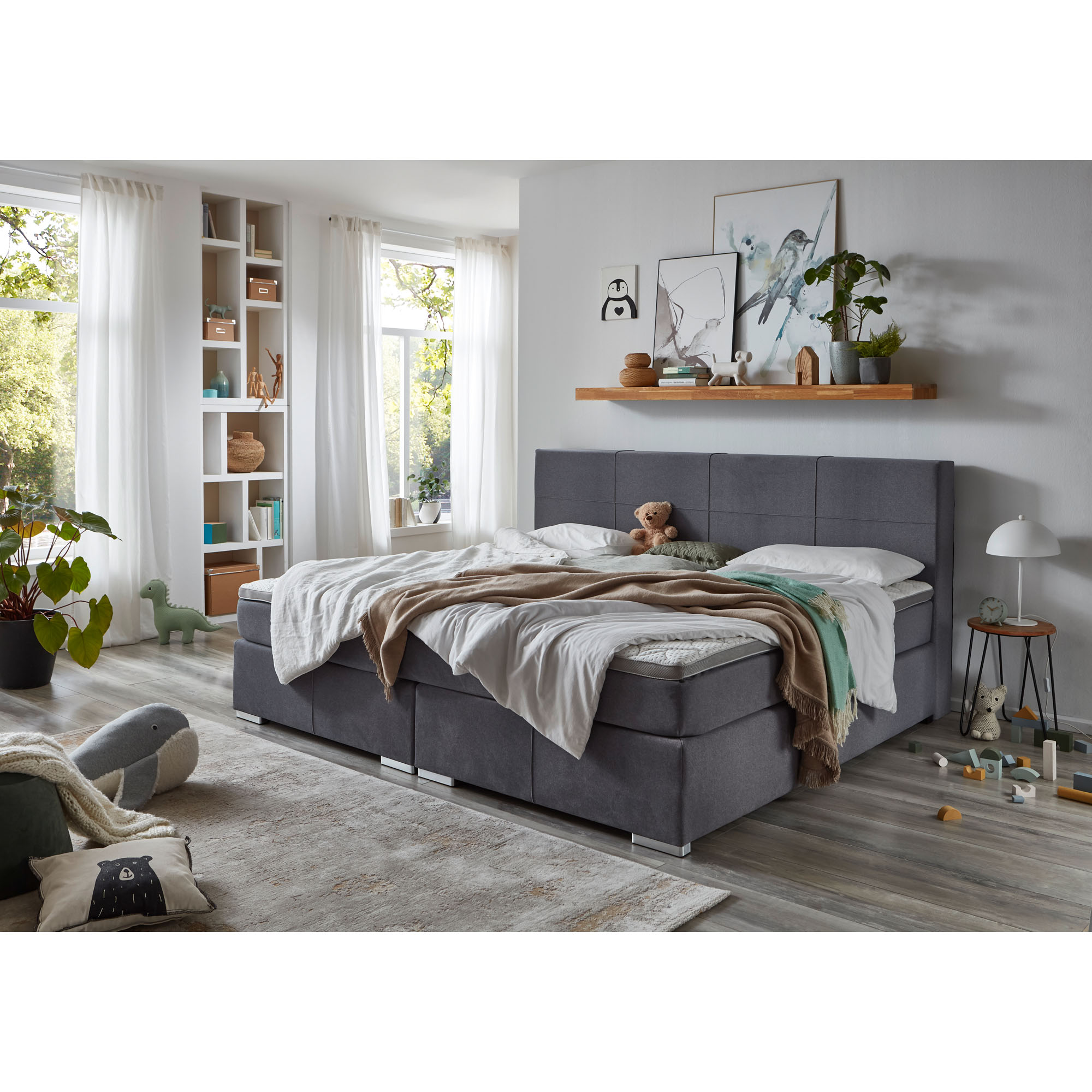 Boxspringbett mit grauem Stoffbezug und Bettwäsche in einem eingerichteten Schlafzimmer