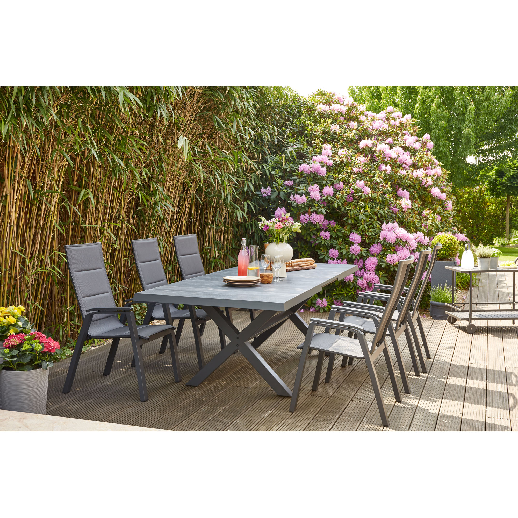Gartenszene mit großem Esstisch und mehreren schwarzen Gartenstühlen aus Aluminium, gedeckter Tisch auf Holzterrasse