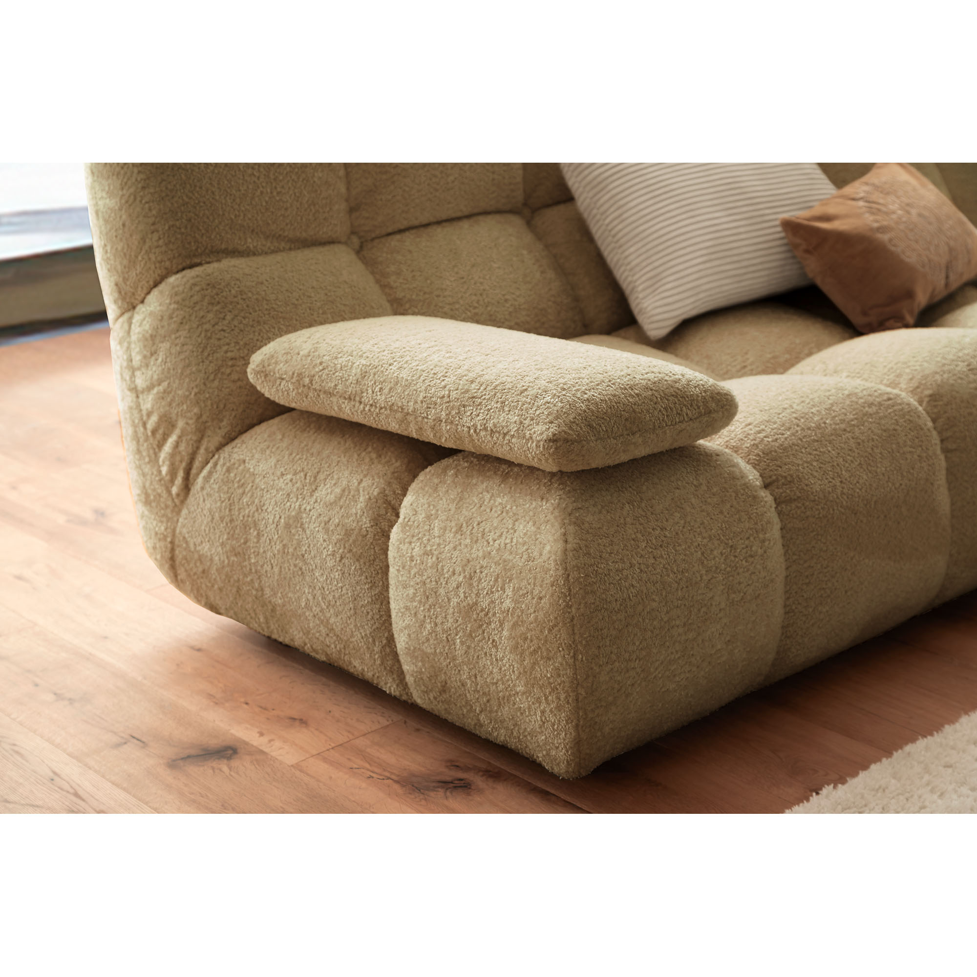 Beigefarbenes Armteilkissen auf der breiten, gepolsterten Armlehne eines Sofas mit abgesteppten Polstern in einem Wohnraum