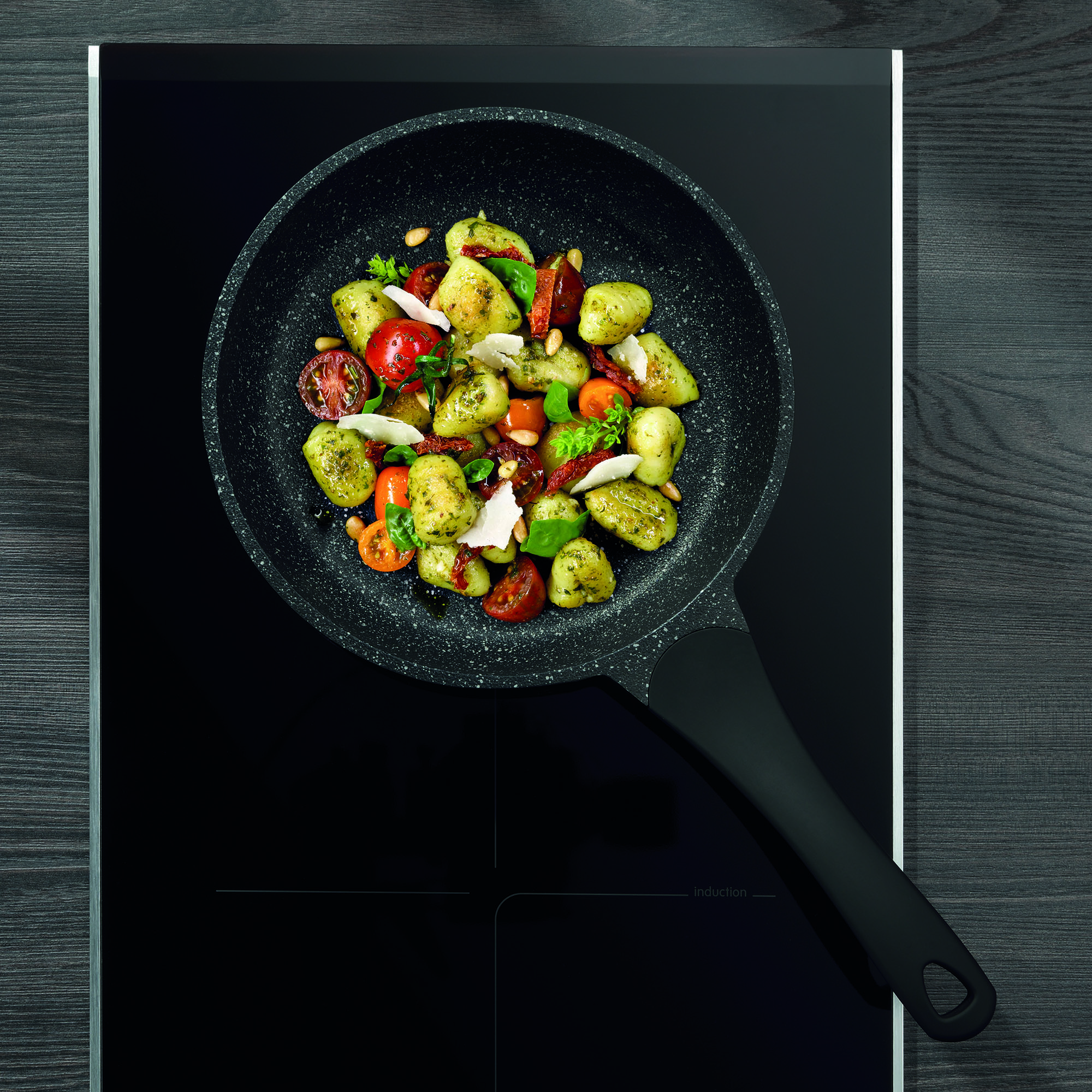 Bratpfanne mit Paprika Zucchini und weiterem Gemüse auf einem dunklen Kochfeld aus der Draufsicht