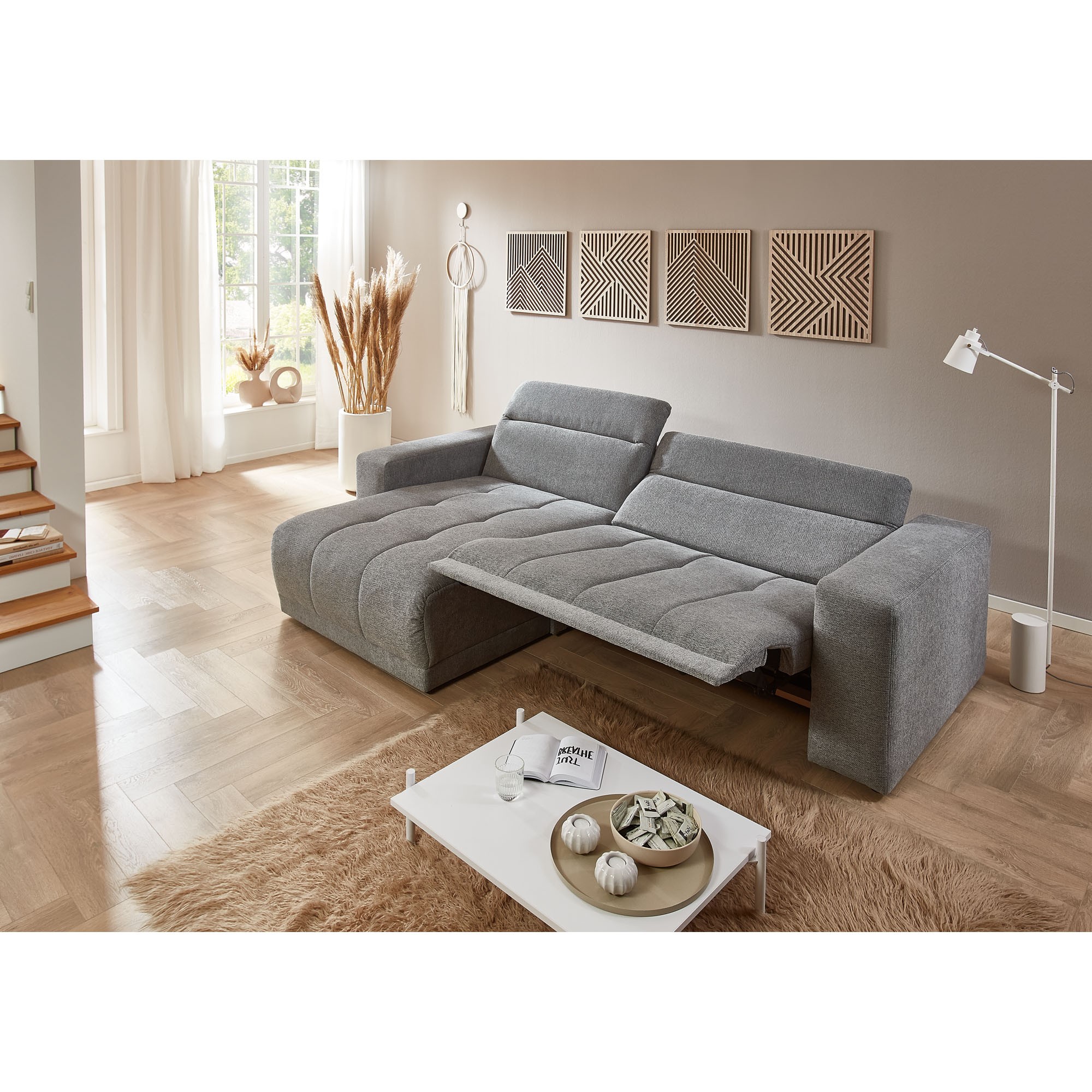 Graues Sofa mit ausgezogener Liegefläche und verstellbarer Rückenlehne im Wohnzimmer mit Holzoptikboden