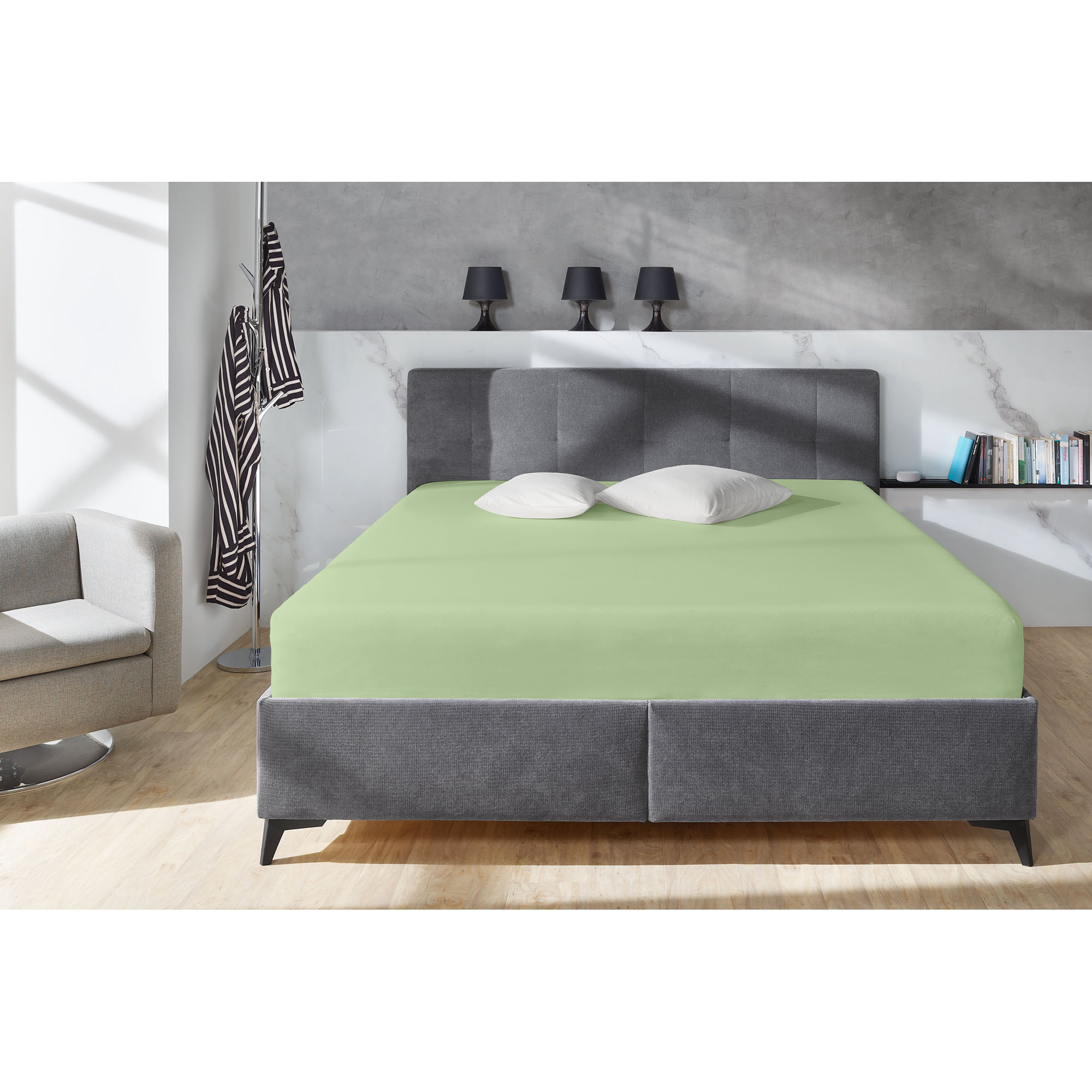 Boxspring-Spannbetttuch in Eukalyptus auf einem grauen Boxspringbett in einem Schlafzimmer; zwei helle Kissen liegen am Kopfende; Größe 150 x 200 x 38 cm.