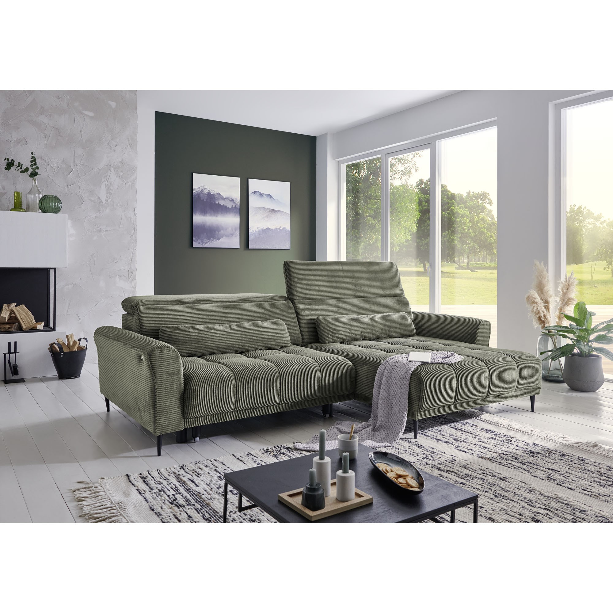 Helles Wohnzimmer mit großem Ecksofa in grünem Cordstoff, dekoriert mit Teppich, Pflanzen und Wandbildern.