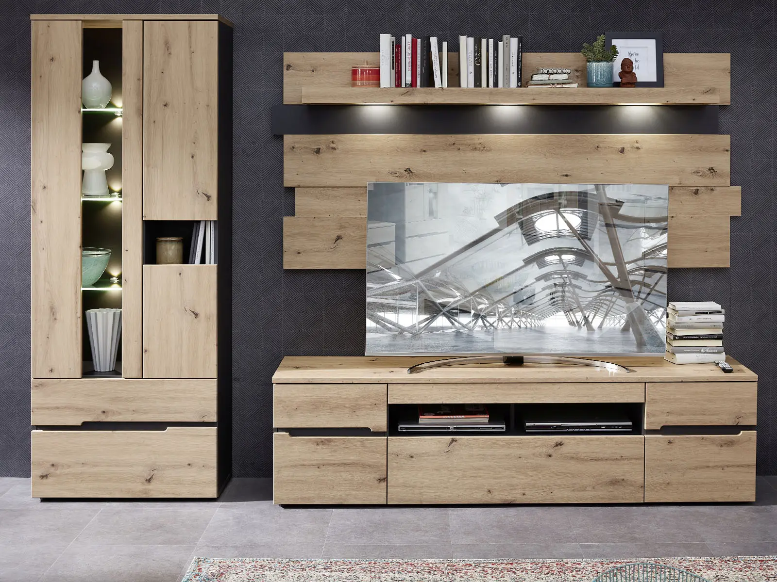 Wohnwand mit hoher Vitrine links sowie TV Lowboard mit Wandpaneel und Regal vor dunkler Wand
