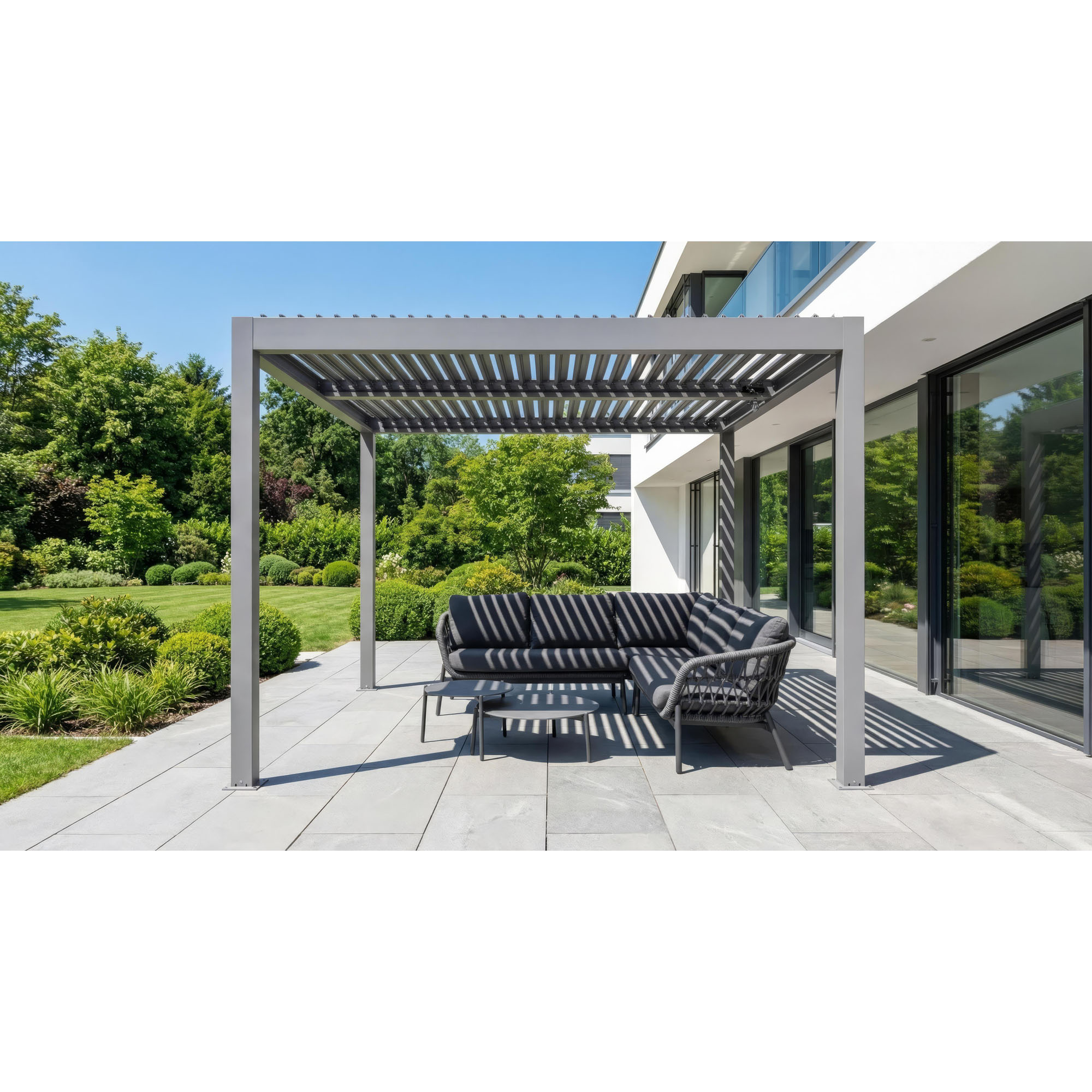 Pergola mit verstellbarem Lamellendach steht über einer Sitzgruppe auf einer Terrasse neben einem modernen Wohnhaus und Garten