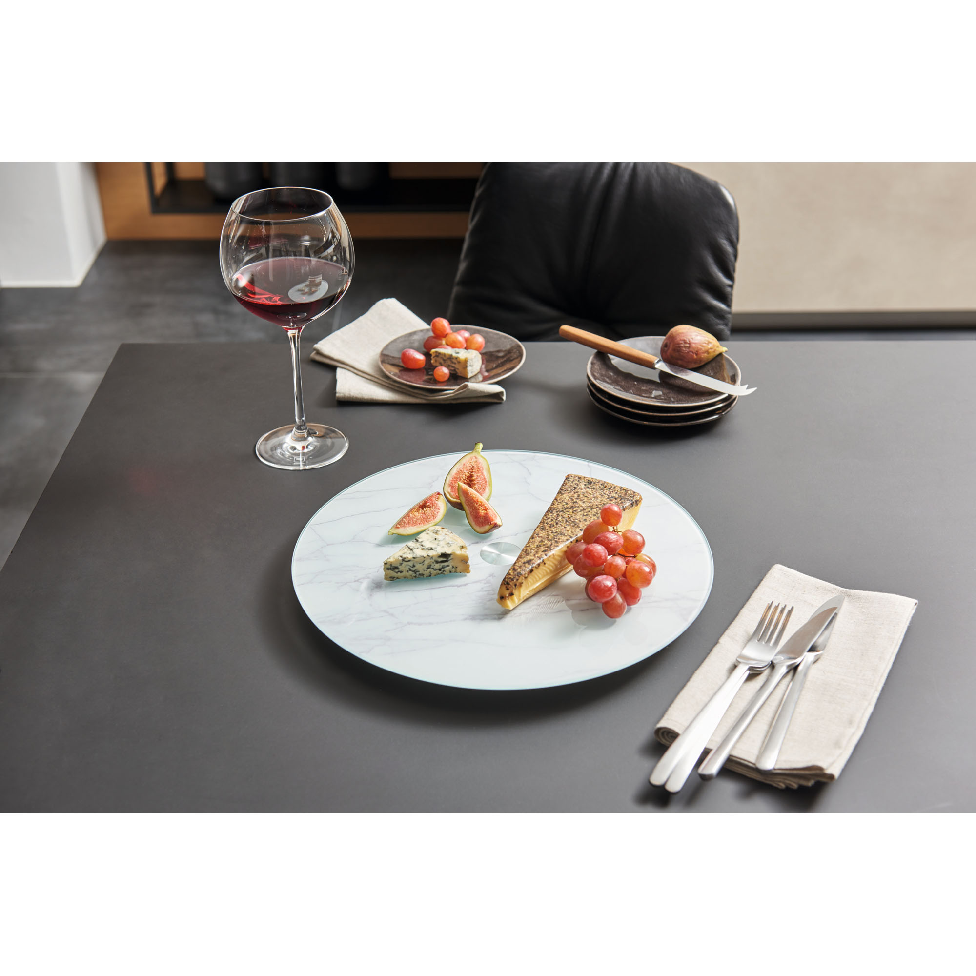 Glas Servierplatte in Marmoroptik mit Käse, Trauben und Weinglas auf Tisch