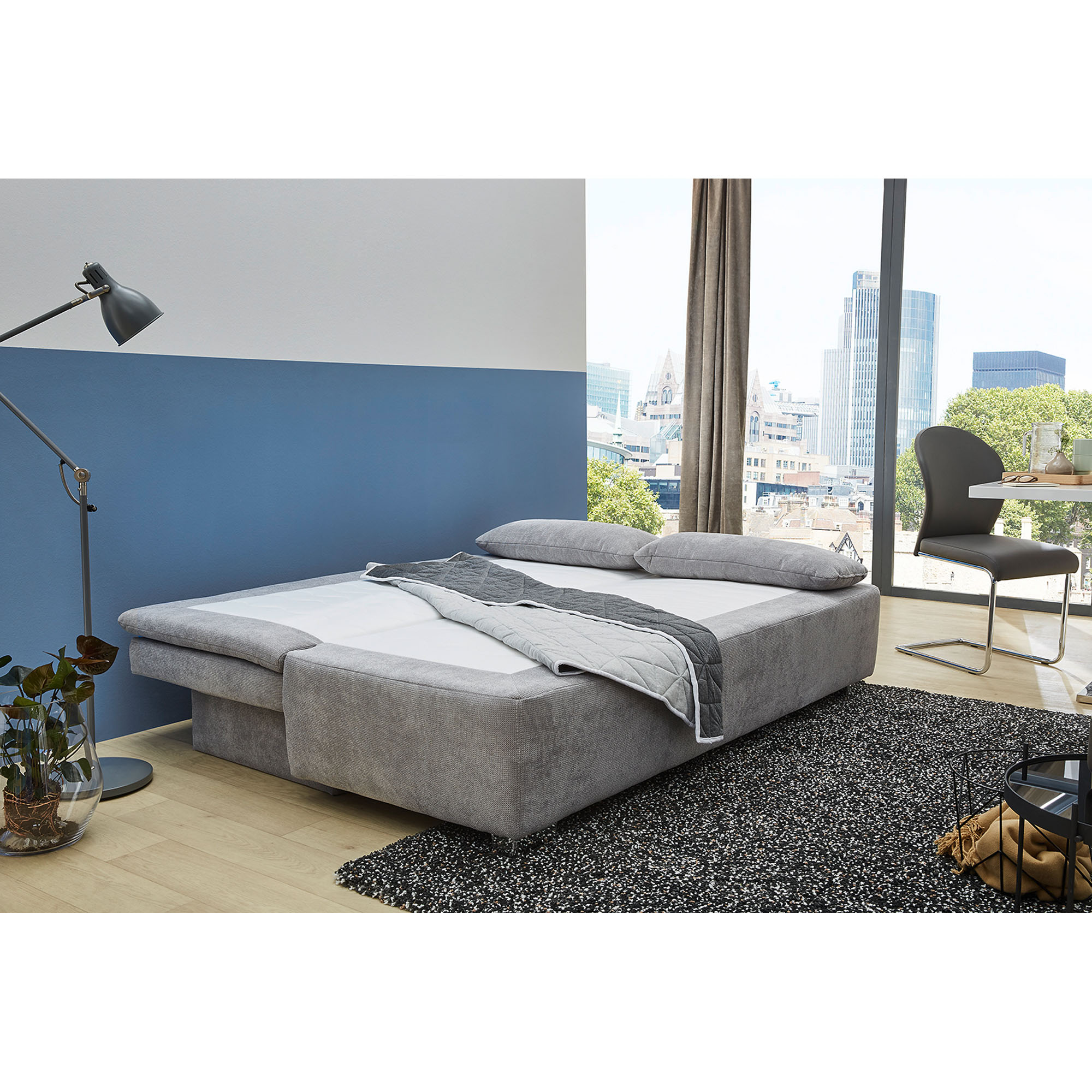 Funktionssofa in Grau, Stellmaß 160x200 cm, mit grauem Kissen, dargestellt in einem Wohnzimmer mit umgeklapptem Bettkasten