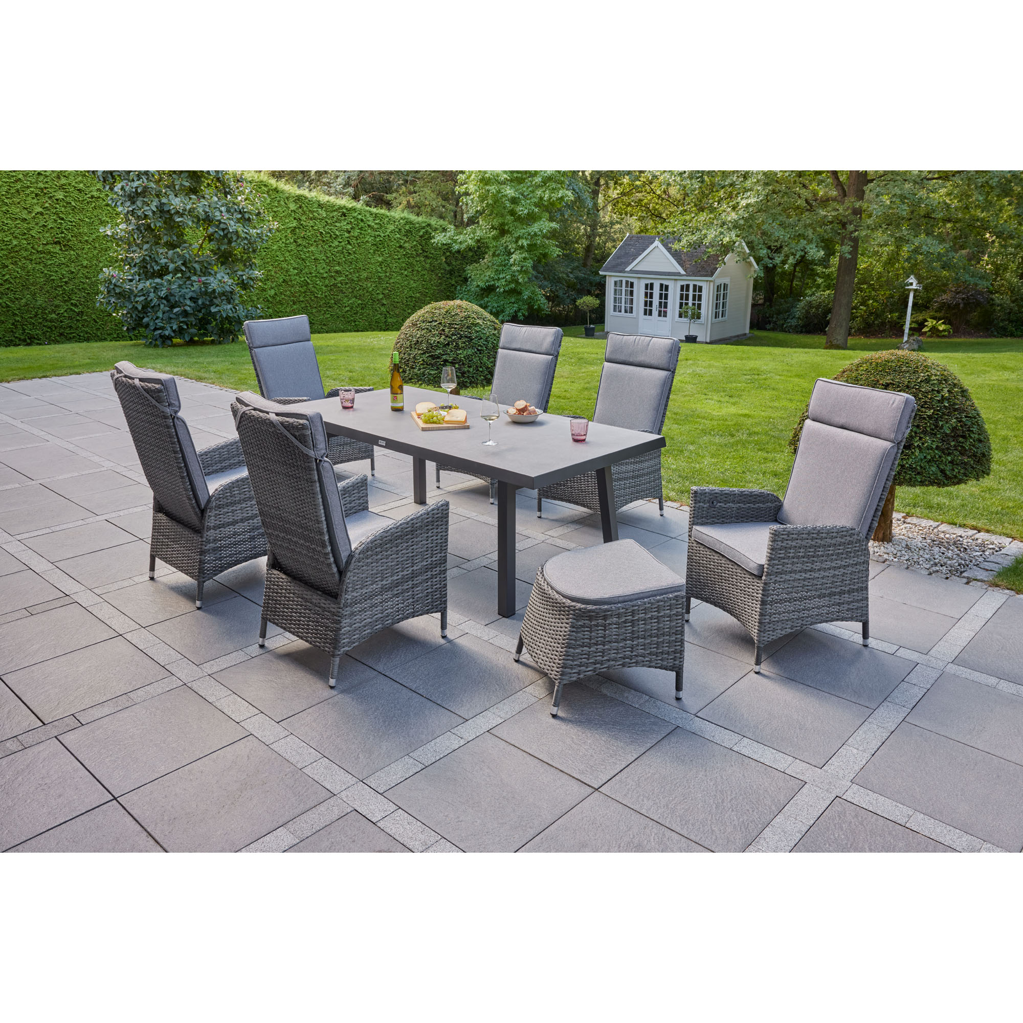 Mehrere Gartenstühle mit Polstern stehen um einen rechteckigen Tisch auf einer Terrasse im Garten