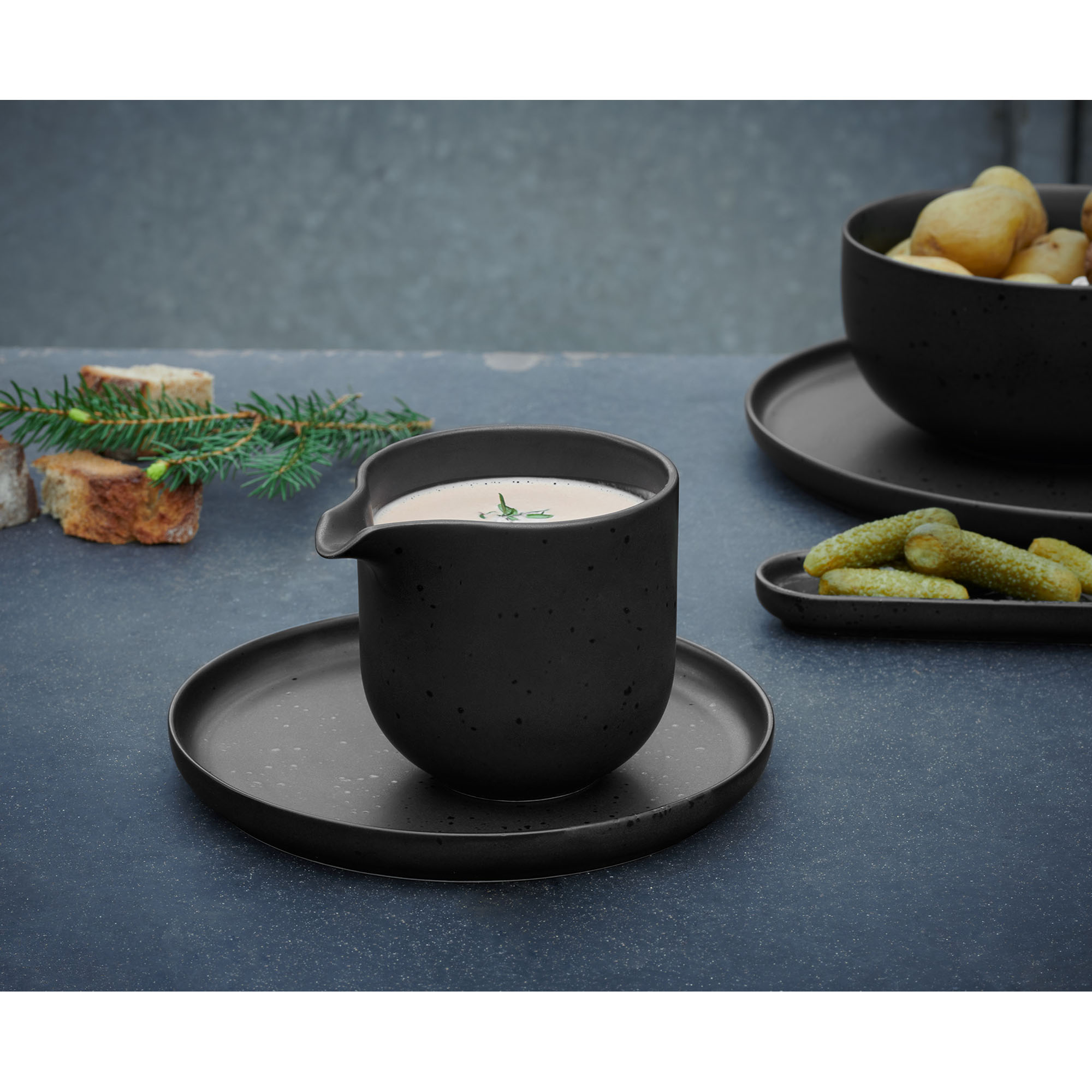 Brotteller der Serie Coppa, Farbe Schwarz matt in einer gedeckten Tischszene mit weiterem Geschirr.