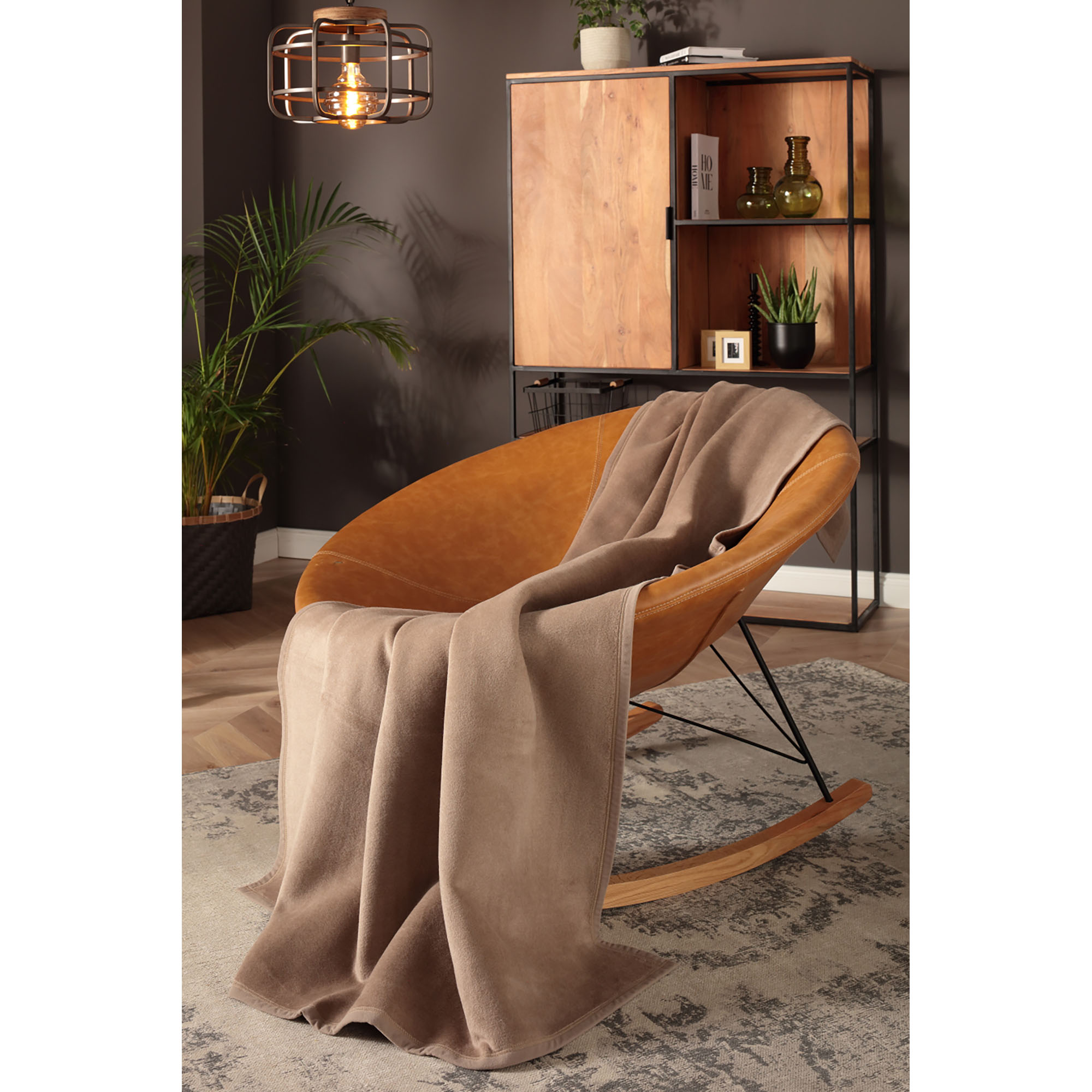 Wohndecke CottonSense palisade hängt über einem cognacfarbenen Loungesessel in einem Wohnraum.