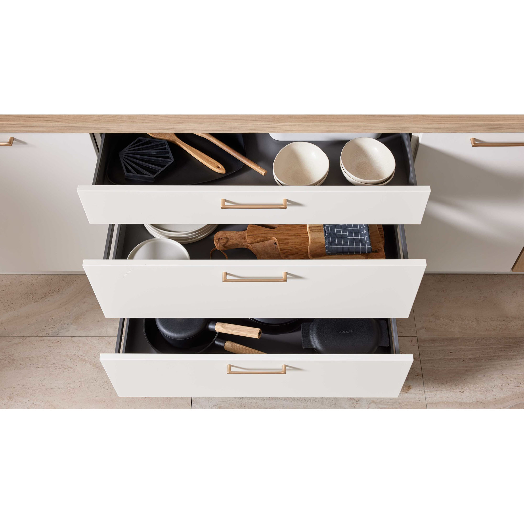Geöffnete Schubladen in heller Küche mit Schüsseln, Schneidebrettern, Pfannen und Kochutensilien