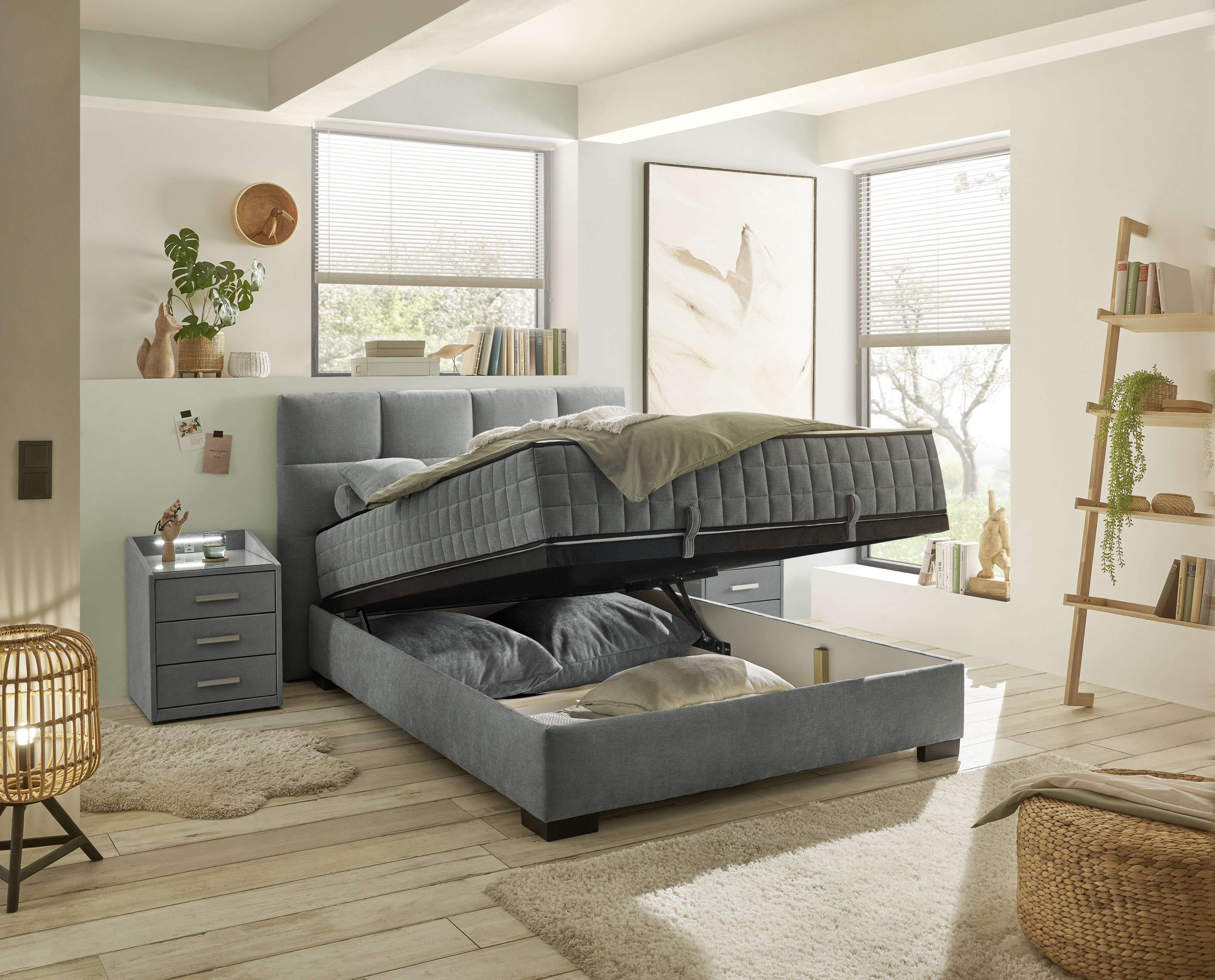 Boxspringbett „Wind 89 anthrazit“ in einem eingerichteten Schlafzimmer, Bettkasten geöffnet, Stauraum im Inneren sichtbar, dekoriert mit Decke und Kissen