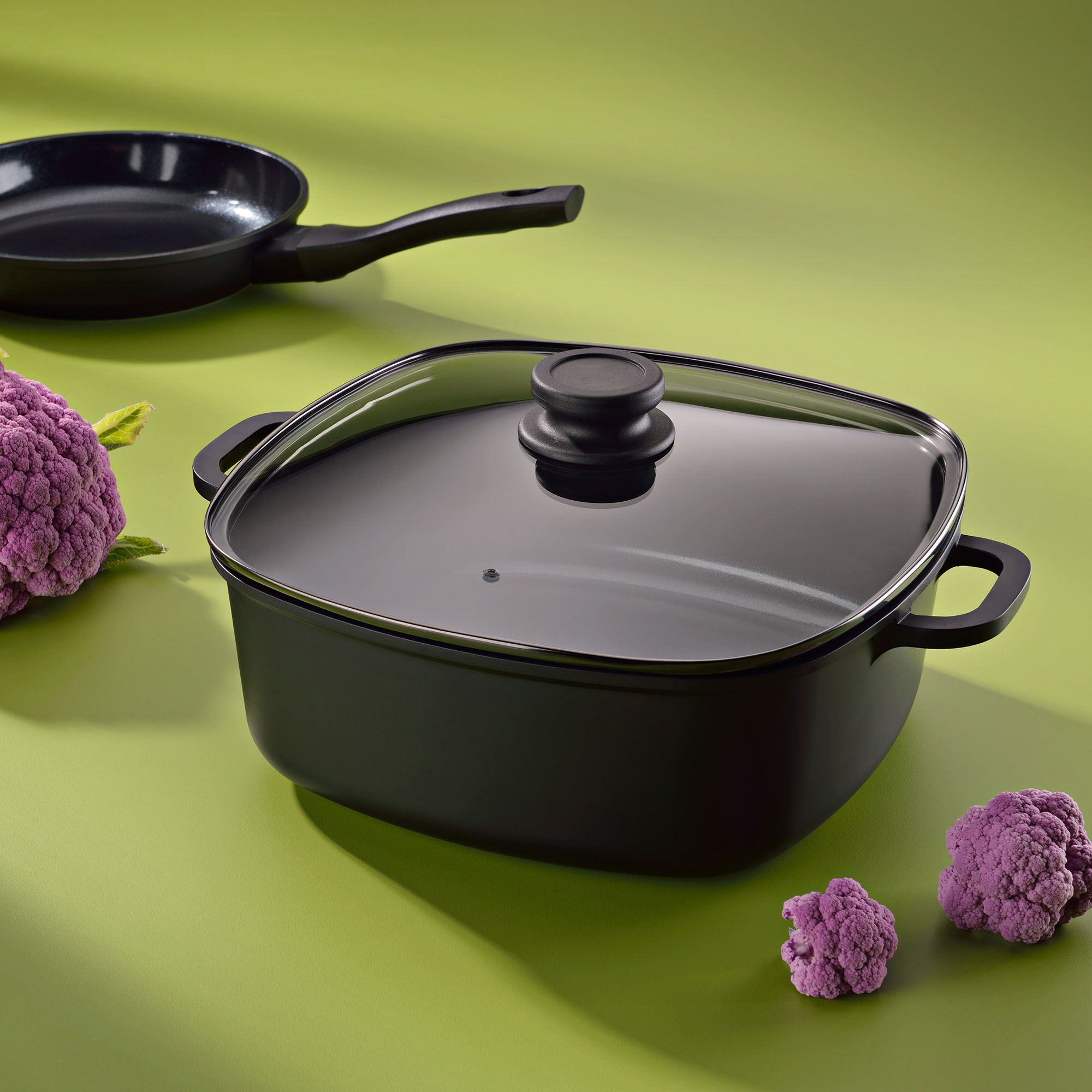 Geschlossene Servierpfanne mit Glasdeckel und zwei Griffen neben violetten Blüten