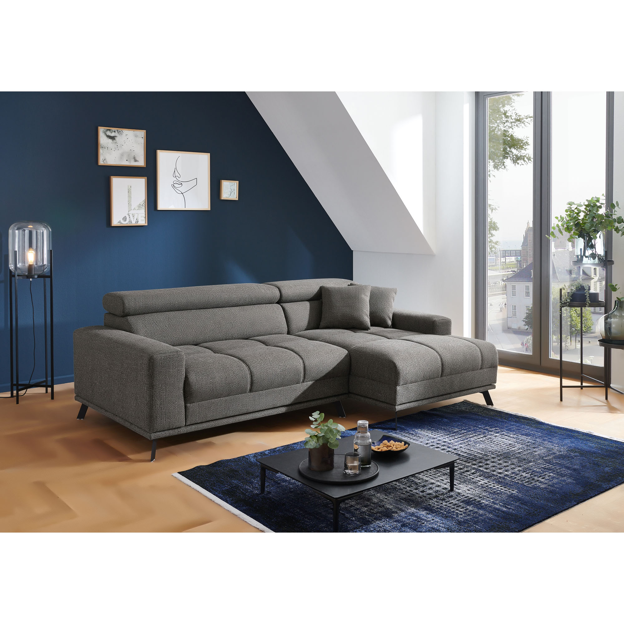 Dunkelgraue Eckcouch mit Longchair rechts im Bild, breiten Armlehnen, zwei grauen Kissen und verstellbaren Kopfstützen im Wohnzimmer