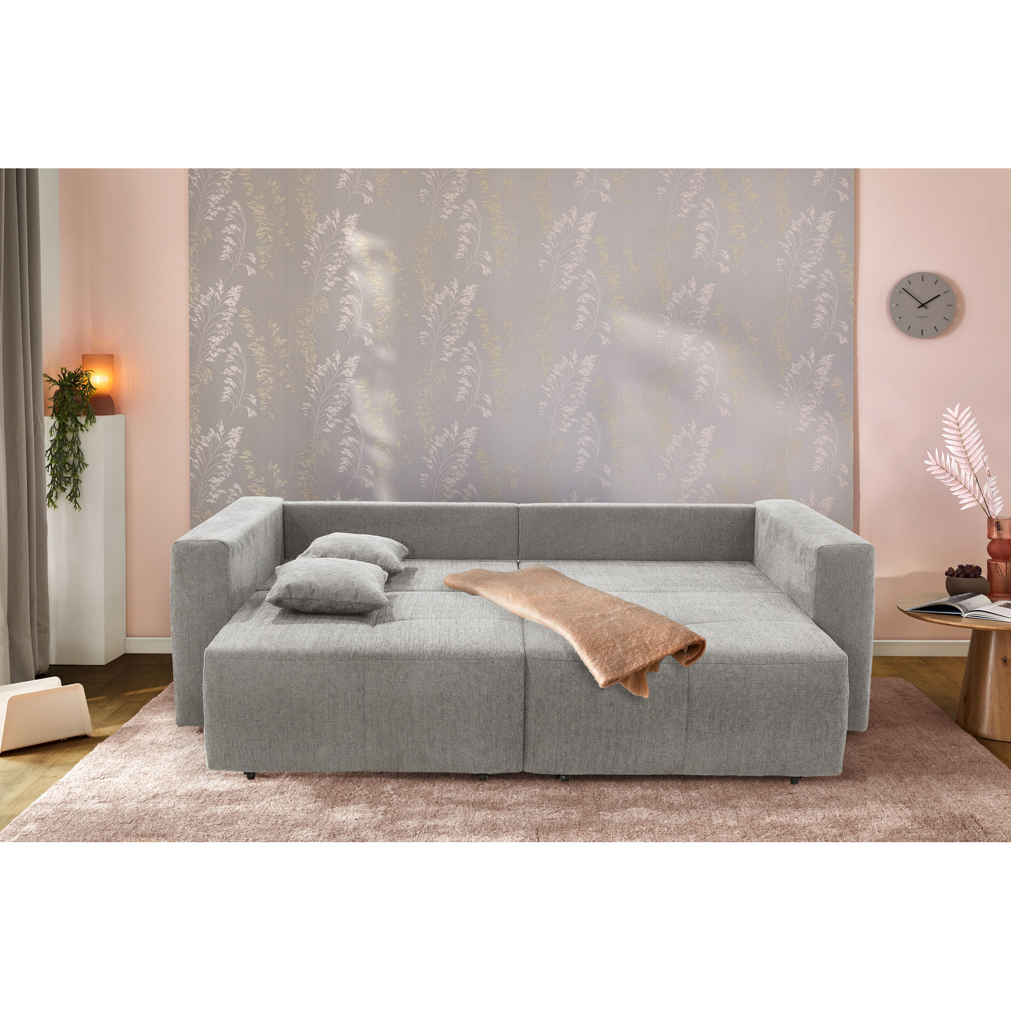 Graues Schlafsofa mit ausgeklappter Liegefläche und Decke in wohnlicher Schlafzimmeroptik
