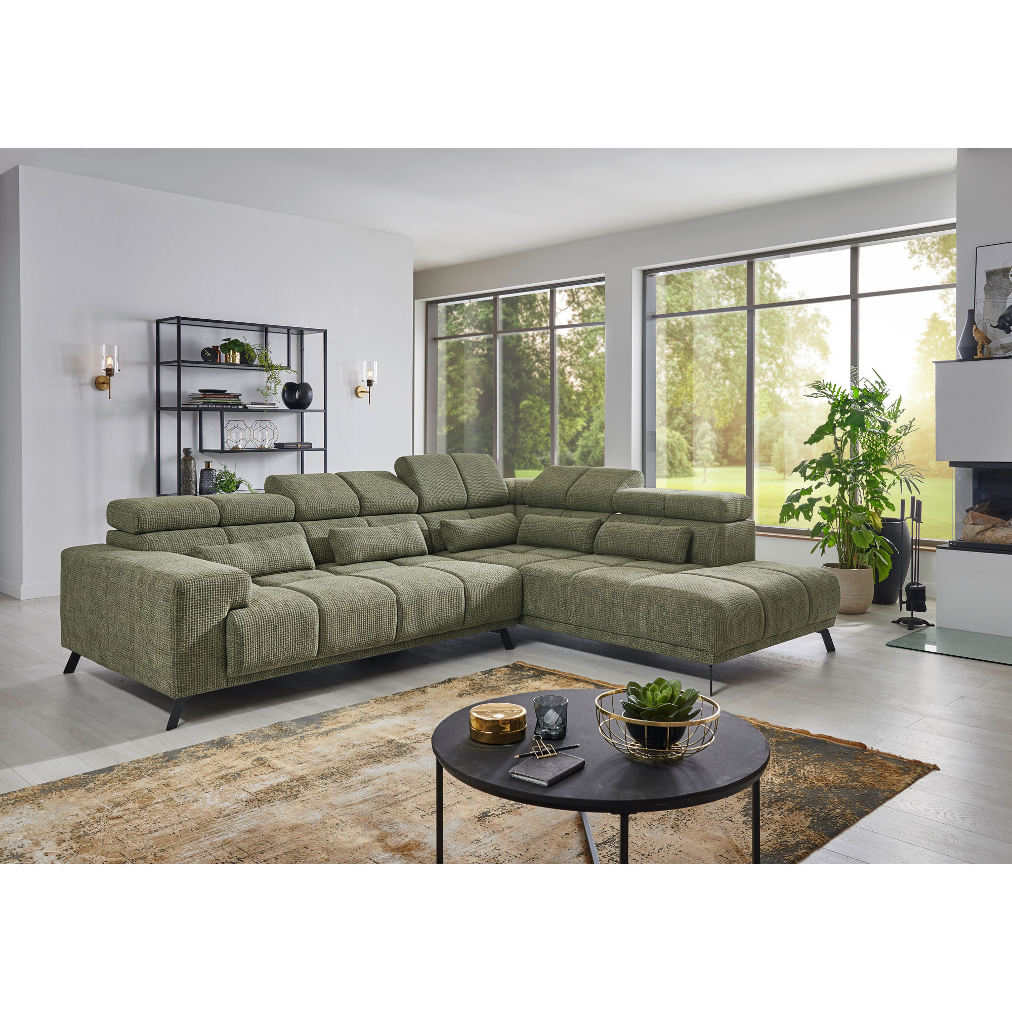 Grünes Ecksofa mit Longchair rechts im Bild, mehreren Kopfstützen, Rückenkissen und schwarzen Metallfüßen in einem hellen Wohnzimmer