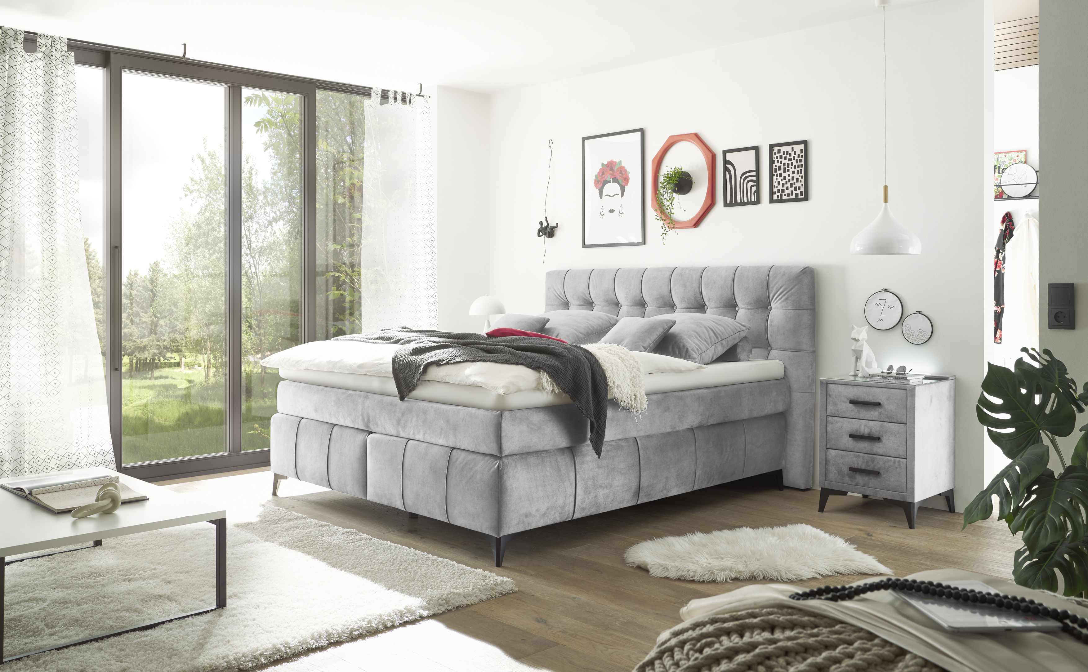 Graues Boxspringbett im eingerichteten Schlafzimmer, dekoriert mit Kissen und Decke, präsentiert in wohnlichem Ambiente