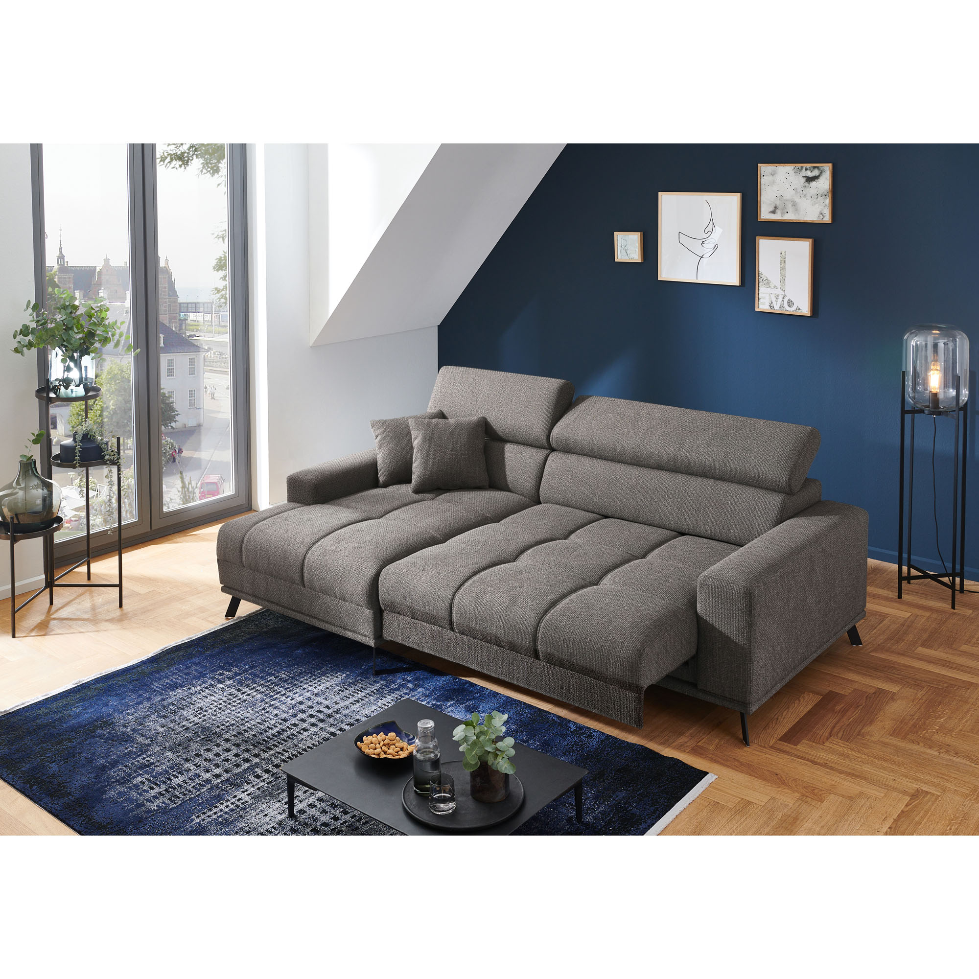 Dunkelgraue Wohnlandschaft mit Longchair links im Bild, ausgezogenen Sitzflächen und aufgestellten Kopfstützen in einem hellen Wohnzimmer