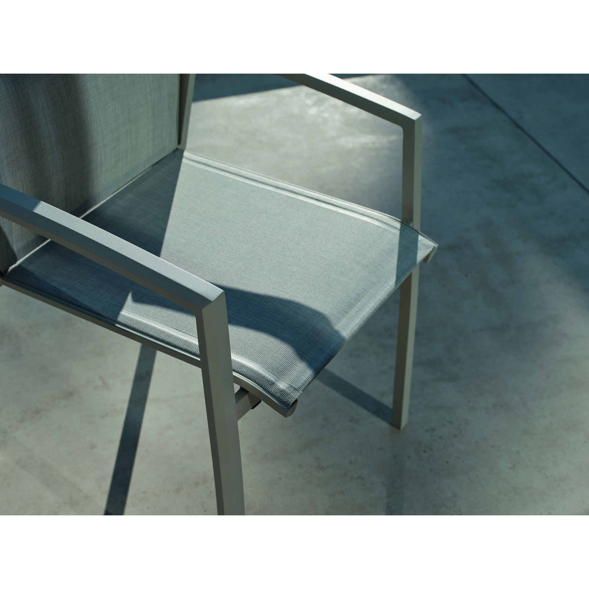 Nahaufnahme der textilen Sitzfläche und Armlehne eines Gartenstuhls, im Schatten und Sonnenlicht auf einer Terrasse.