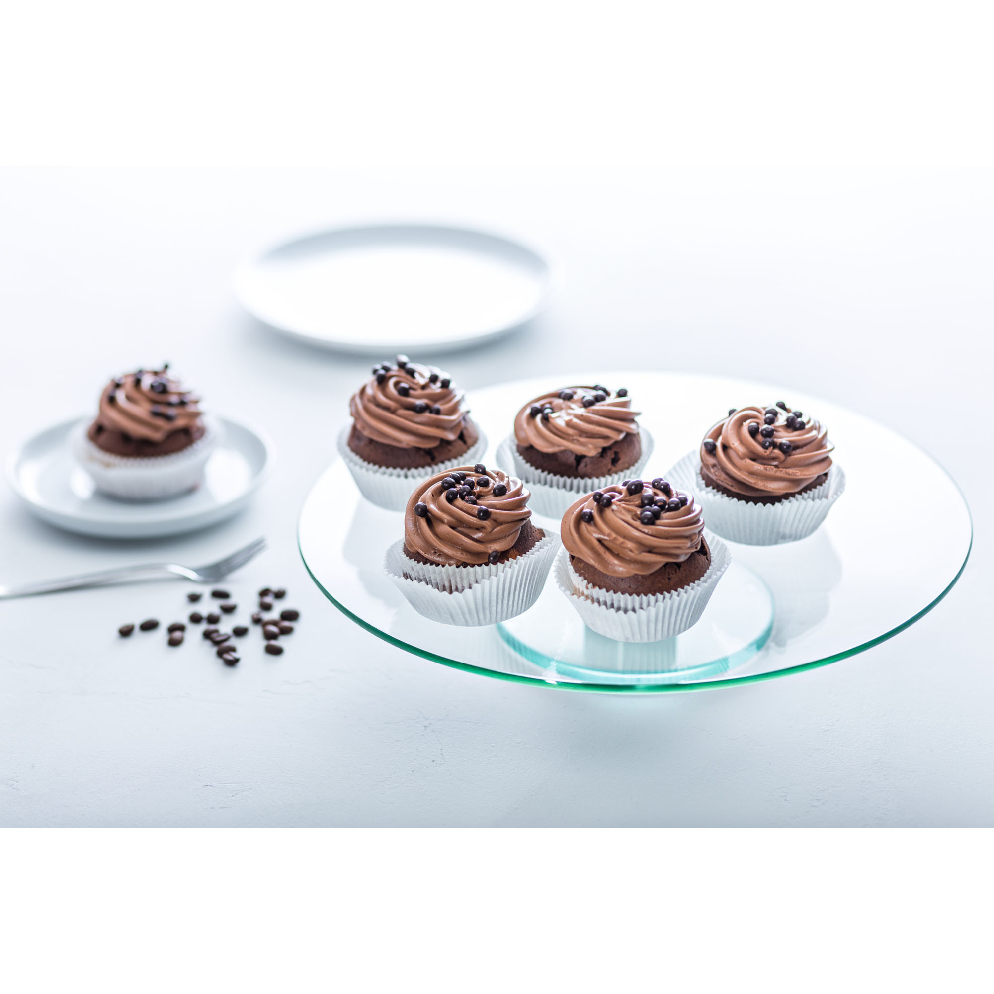 Glas-Tortenplatte dekoriert mit mehreren Cupcakes auf weißem Hintergrund