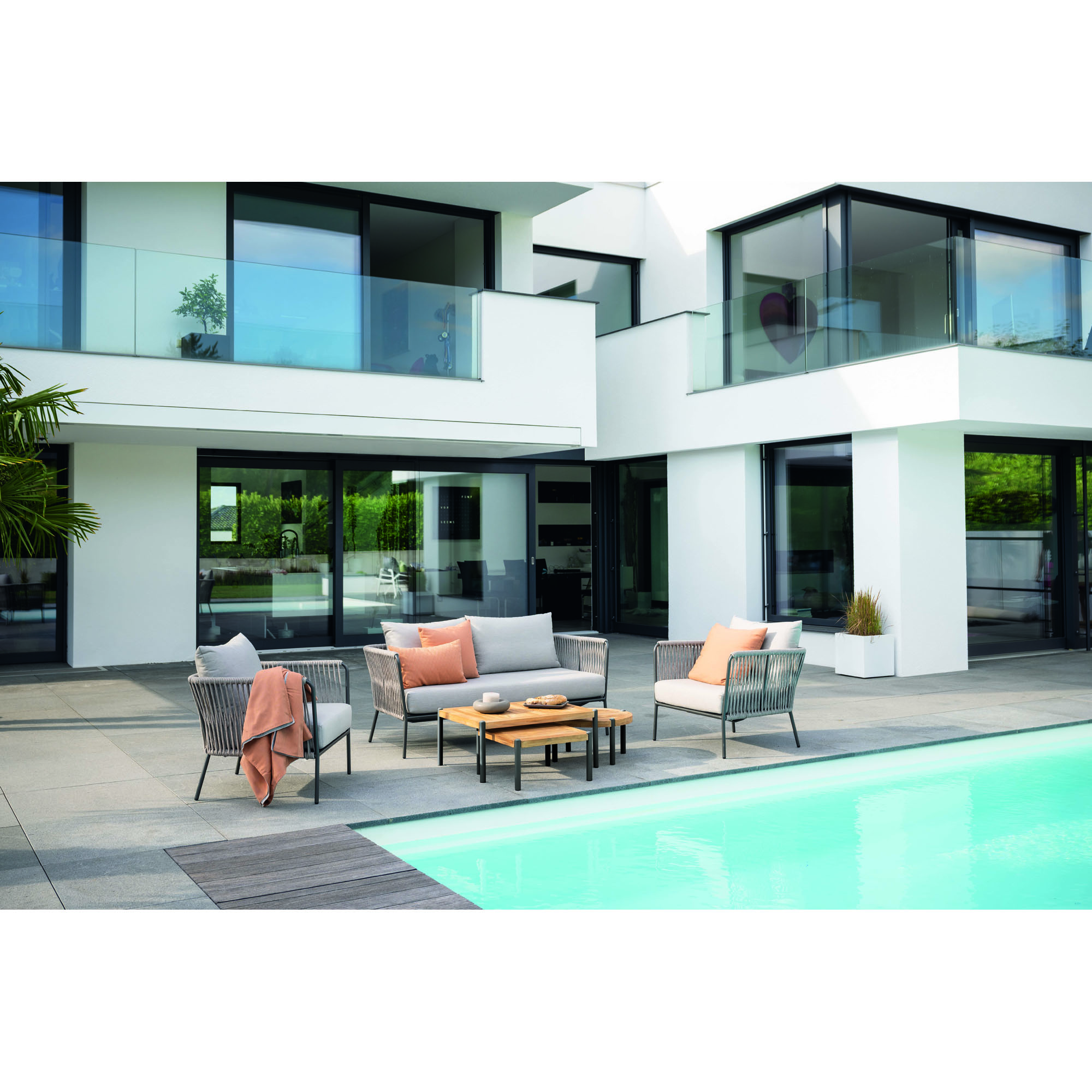 Gartensitzgruppe mit Tisch und Sitzmöbeln auf einer Terrasse vor einem modernen Wohnhaus mit Pool