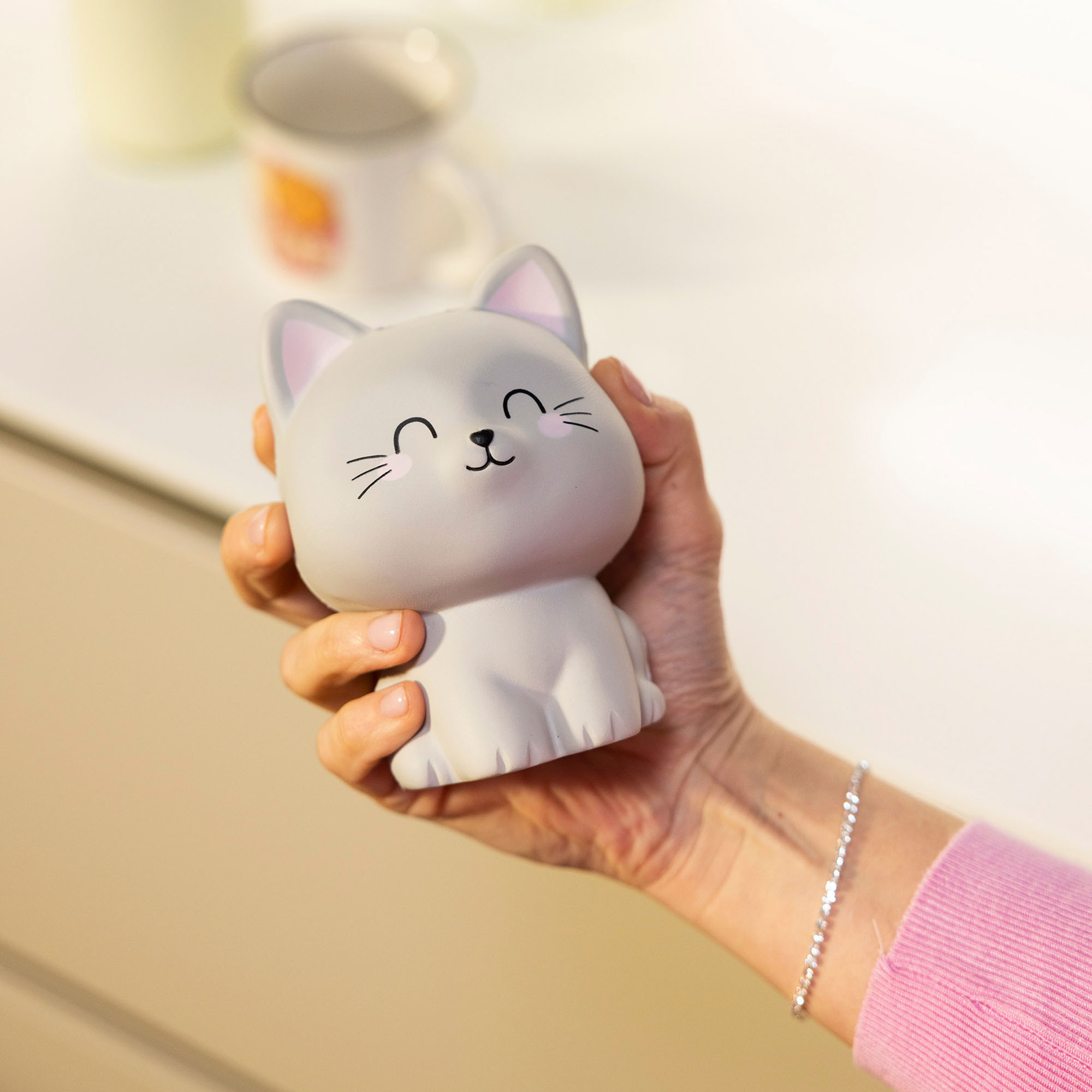 Graue Antistress-Figur in Katzenform, frontal auf einer geöffneten Handfläche gezeigt.