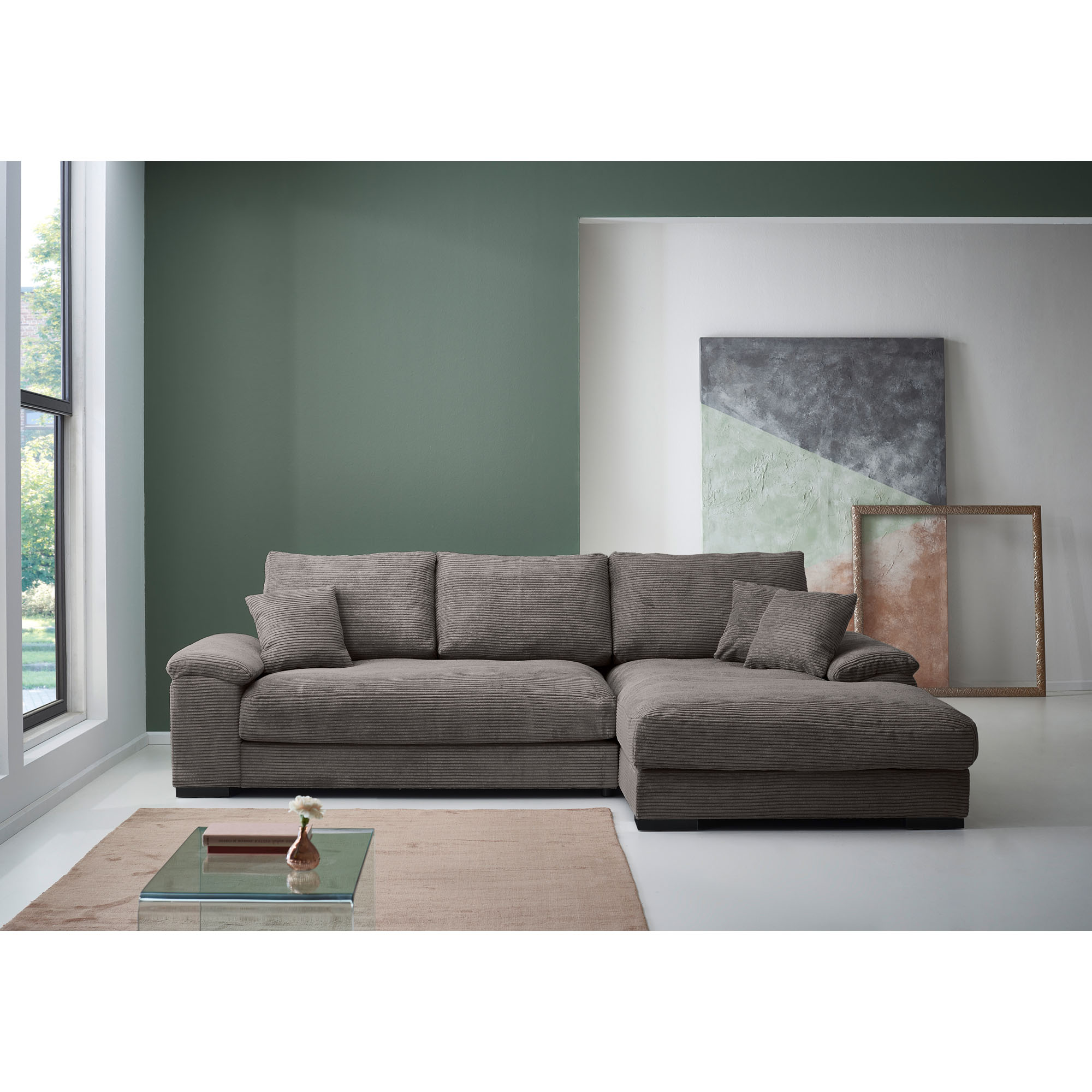 Braune Eckcouch aus Cord mit Longchair rechts im Bild, weichen Rückenkissen und gepolsterten Armlehnen vor einer grünen und weißen Wand
