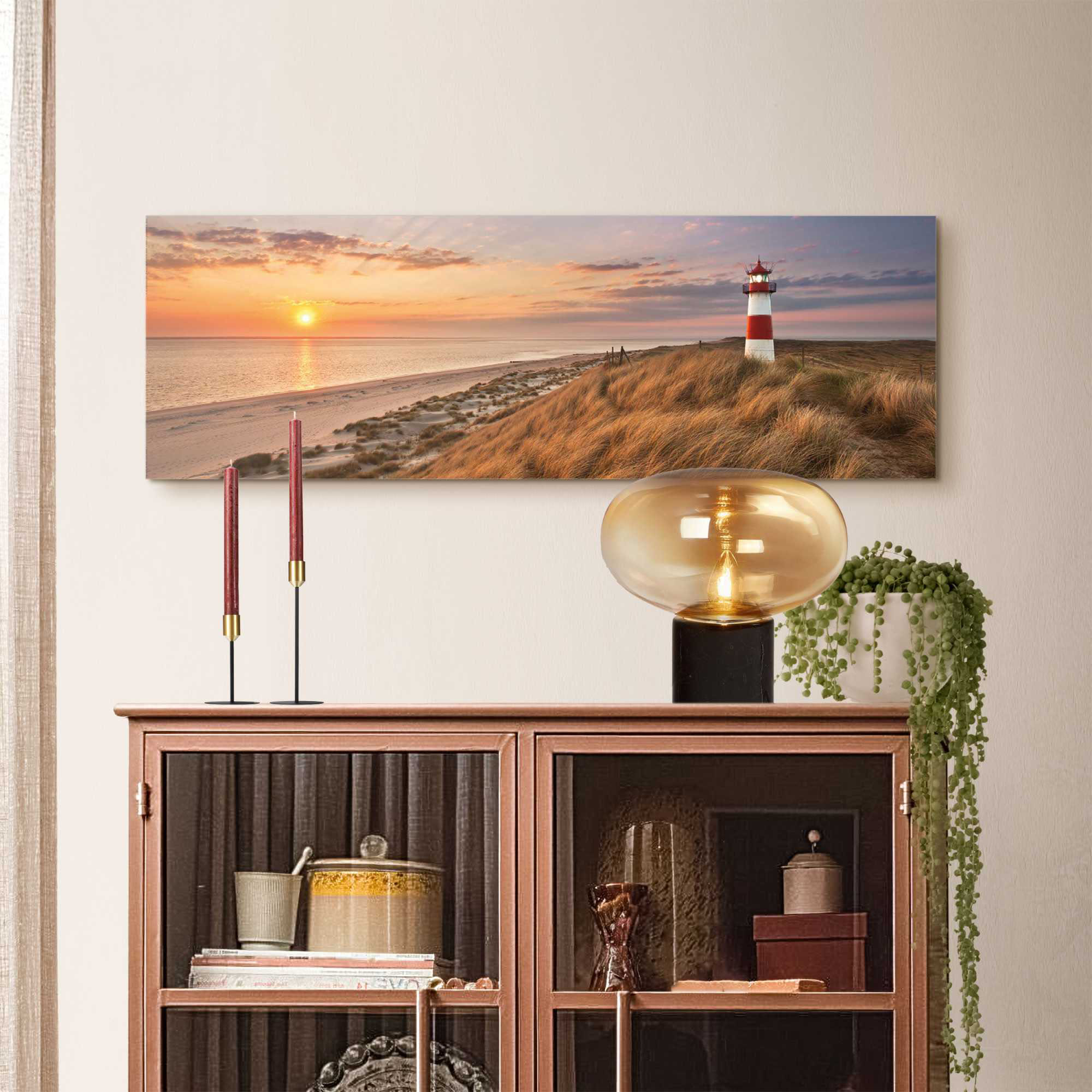 Das Wandbild „Lighthouse Sunset“ in Beige, 30 × 90 cm, hängt in einem eingerichteten Wohnraum und zeigt die Größenwirkung an der Wand.