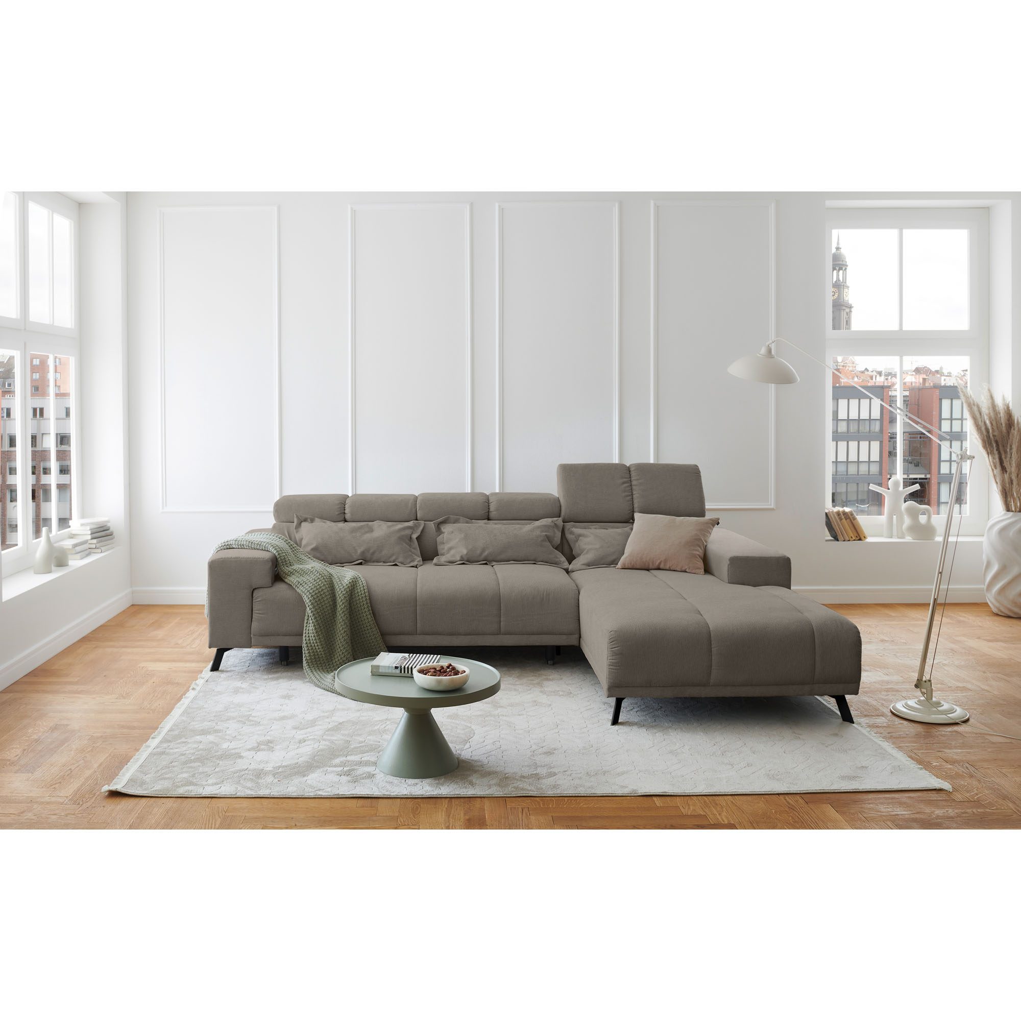 Hellgraues Ecksofa mit Ottomane rechts, verstellbaren Kopfstützen und Rückenkissen in einem hell eingerichteten Wohnzimmer