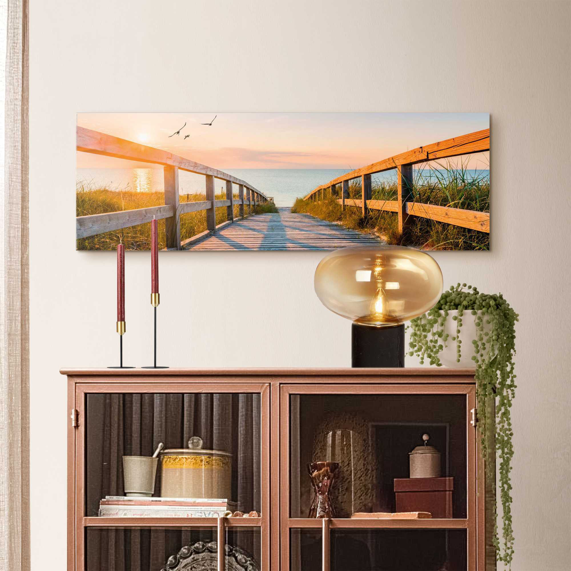 Das Wandbild „Beach Boardwalk“ in Orange, 30 × 90 cm, hängt in einem eingerichteten Wohnraum und zeigt die Größenwirkung an der Wand.