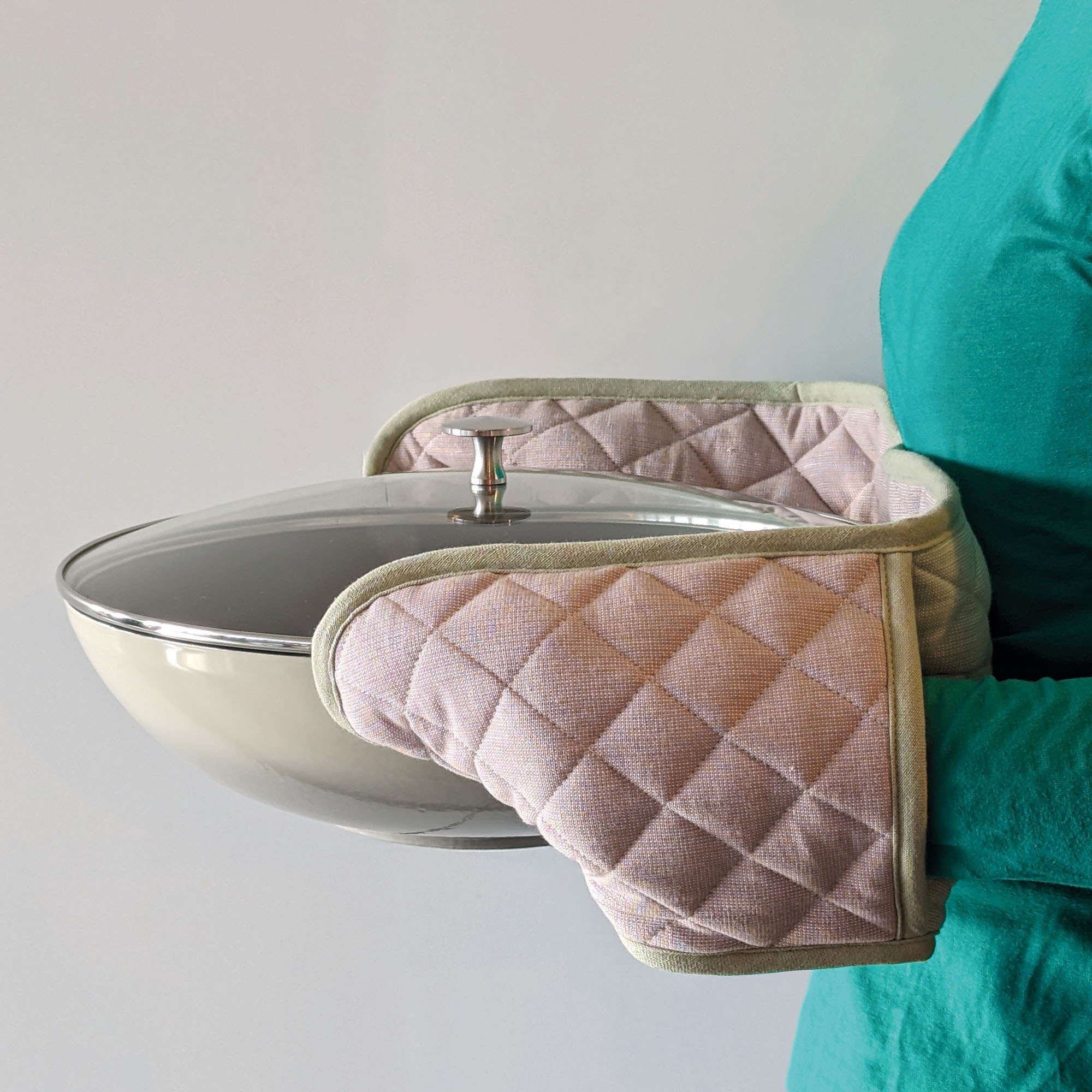 Eine Person hält einen heißen Metalltopf mit dem doppelten Ofenhandschuh an beiden Griffen