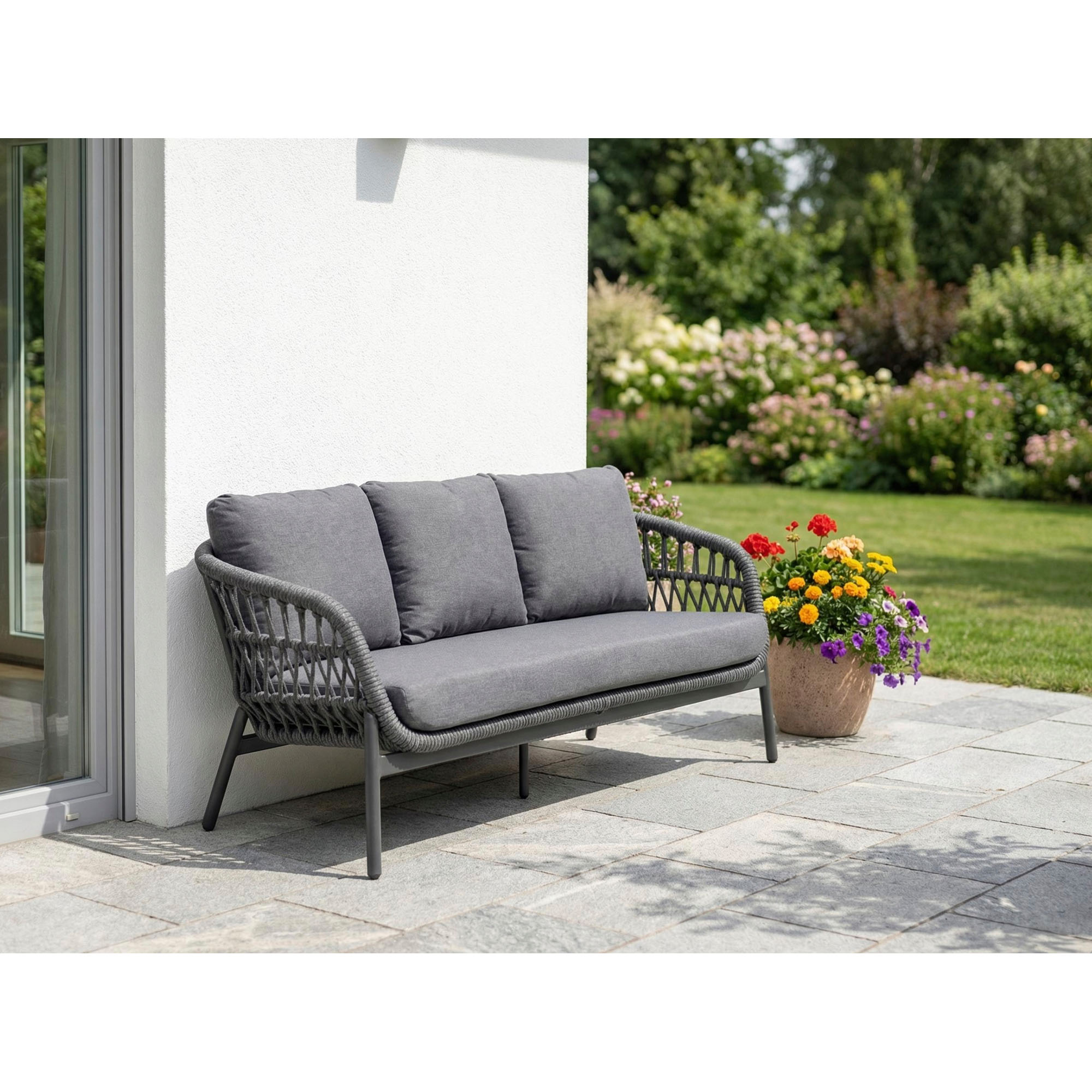 graues Gartensofa steht auf einer Terrasse vor einer Hauswand daneben stehen Pflanzen und ein Blumentopf