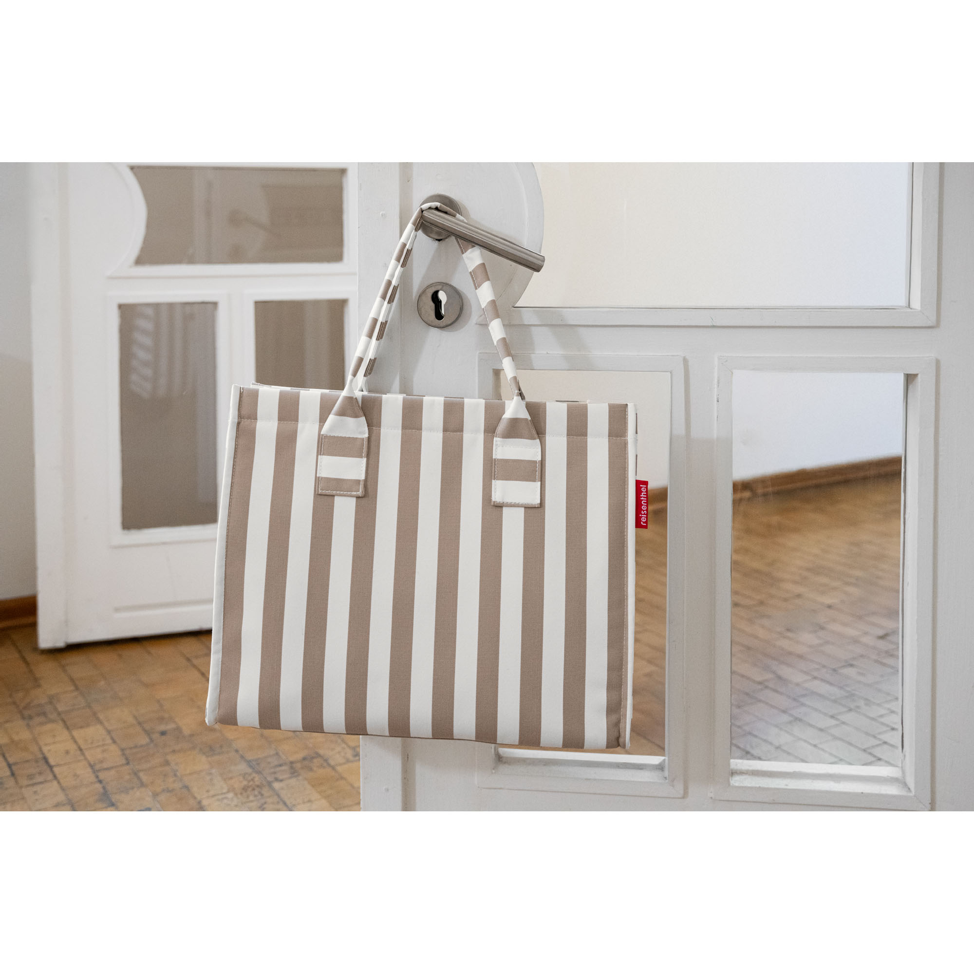 Beige-weißer Reisenthel Shopper mit Streifenmuster hängt an einem silbernen Türgriff in einem hellen Raum