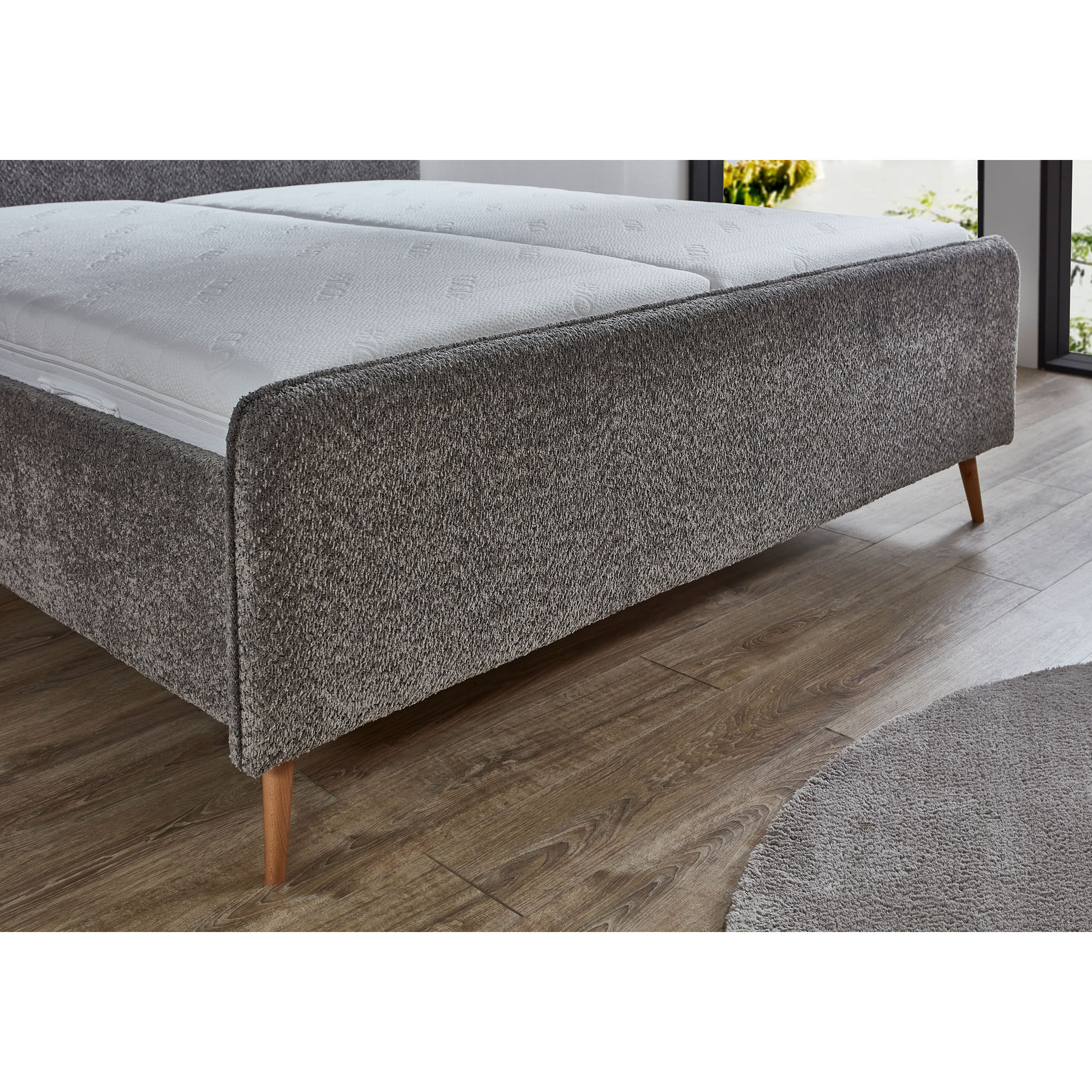 Polsterbett mit grauem Stoffbezug und Holzfüßen mit eingelegter Matratze im Schlafzimmer