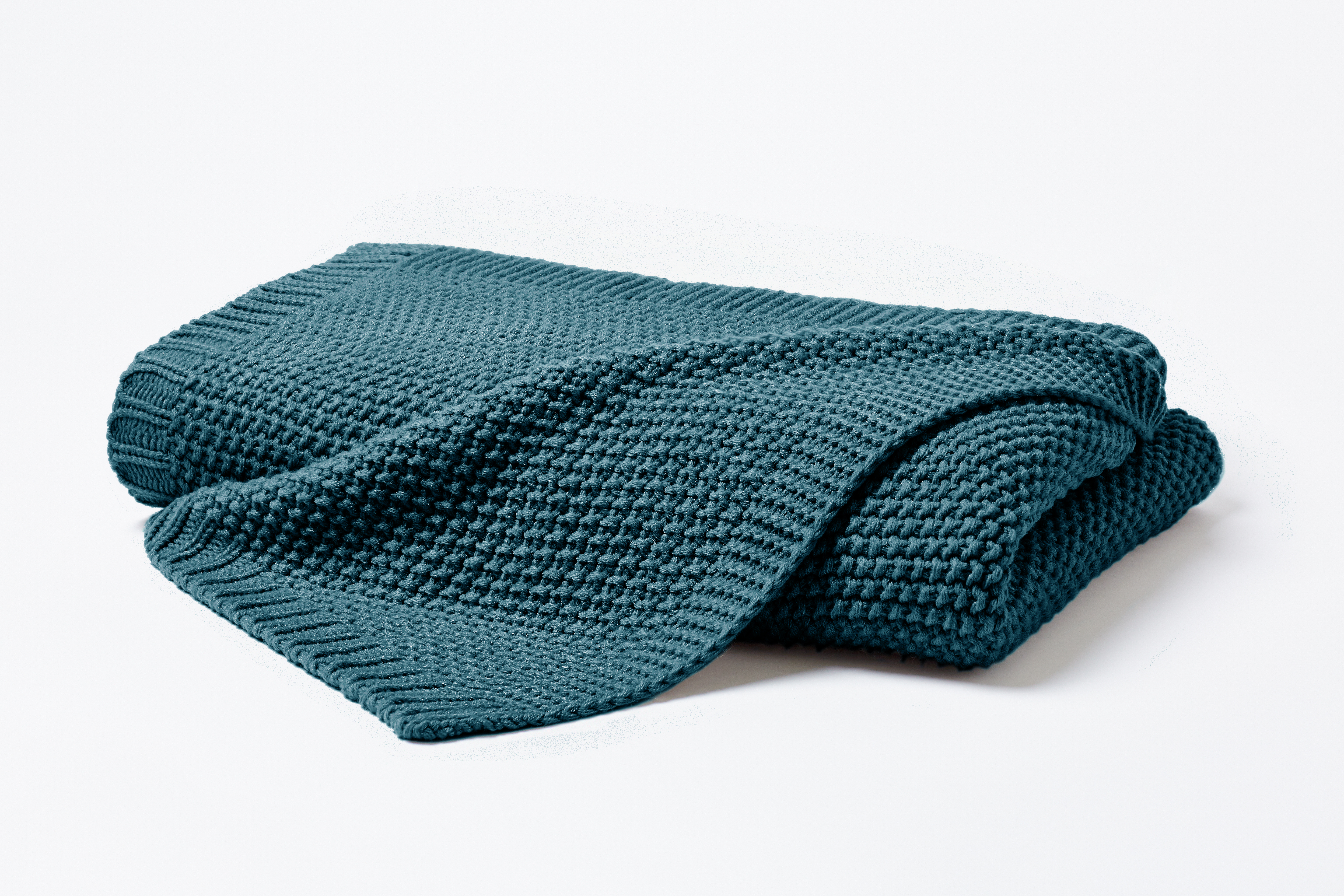 Gefaltete Strickdecke in Smaragd mit locker übergelegter Ecke; die grobe Waffelstrickstruktur ist vor hellem Hintergrund erkennbar; Größe 130 x 170 cm.