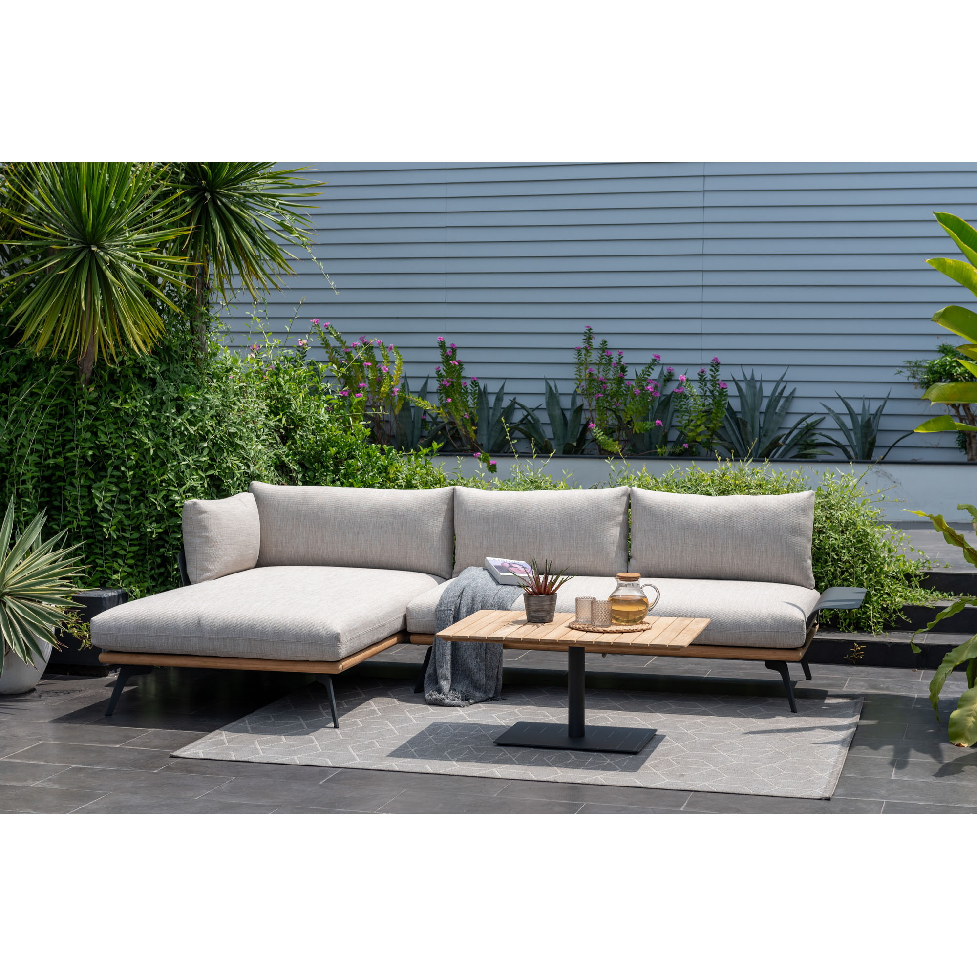Garten Loungegruppe mit Ecksofa, Liegeelement und Tisch auf einer Terrasse mit Pflanzen und Teppich