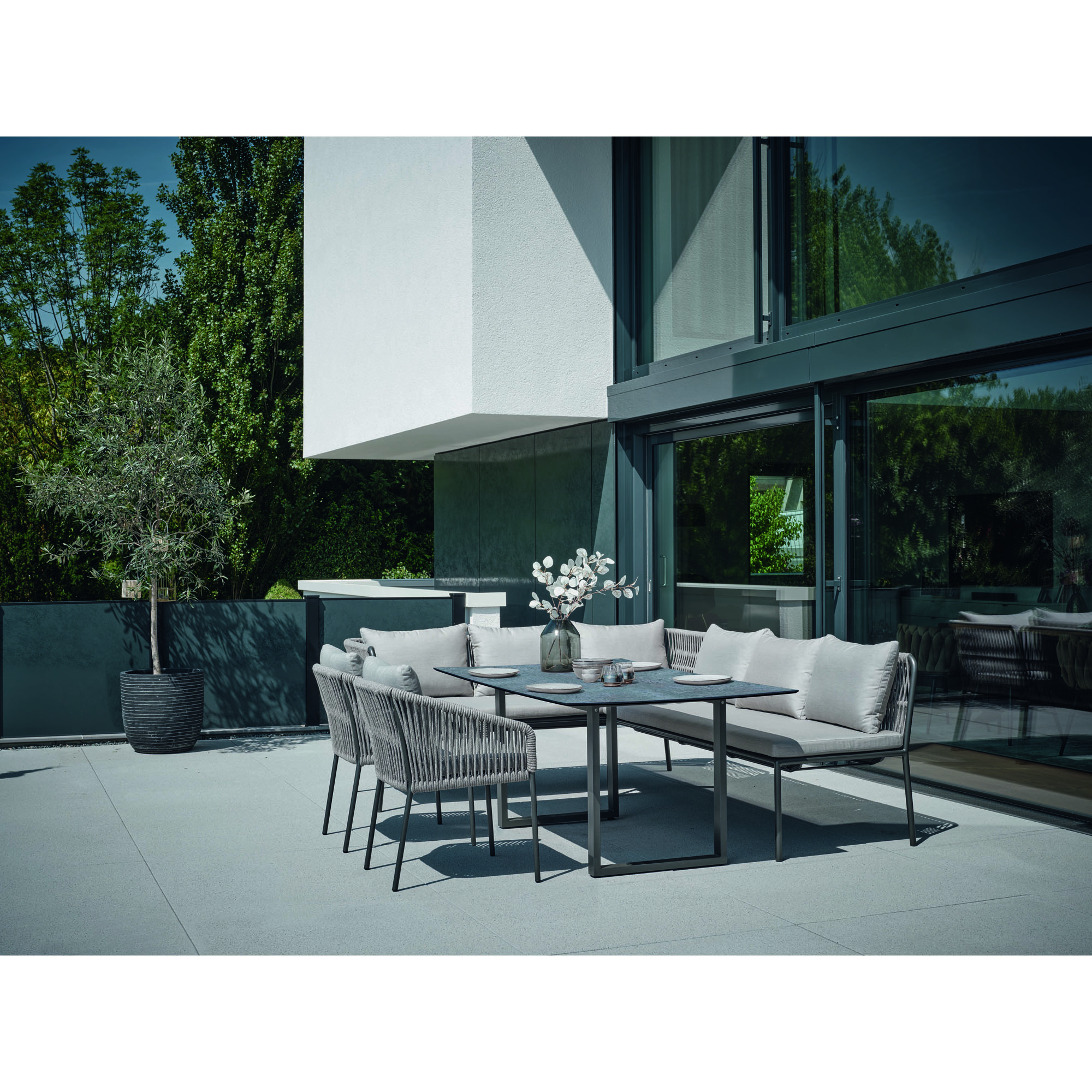 Eine alternative Ansicht einer Sitzgruppe aus Gartenbänken und Stühlen auf einer Terrasse vor einem modernen Gebäude.