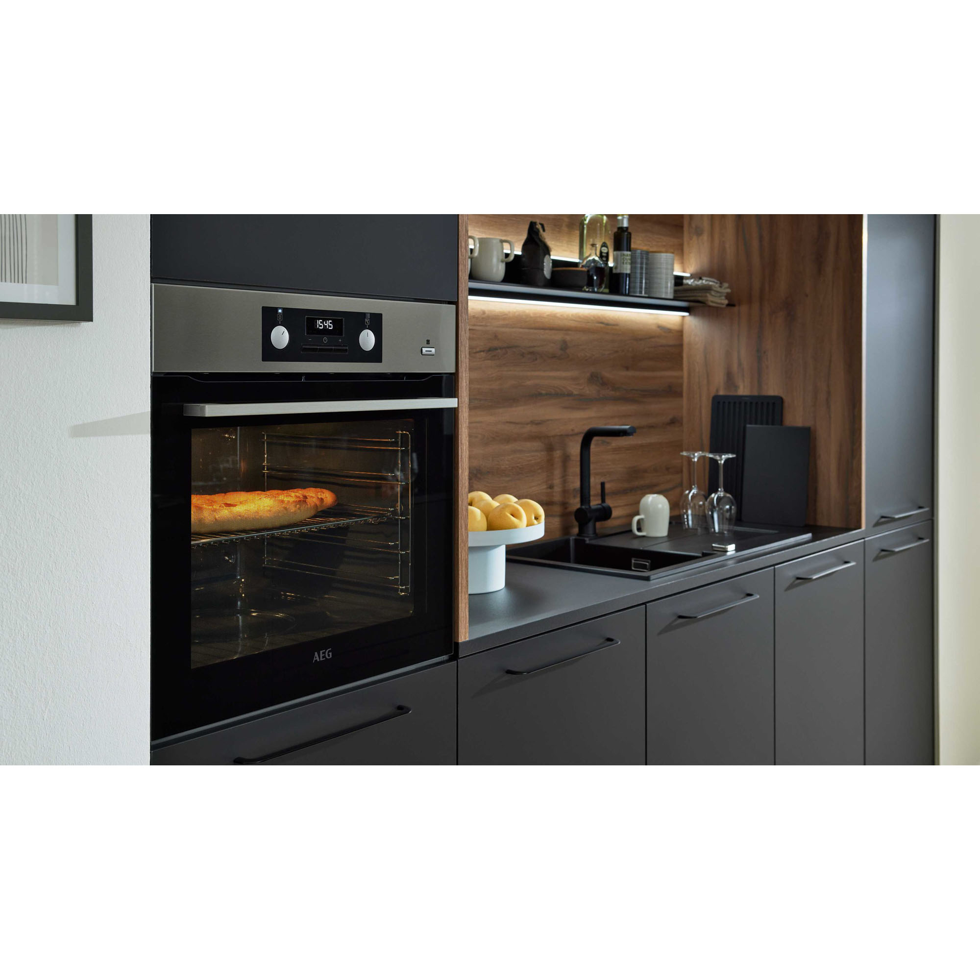 Nahaufnahme eines Backofens neben einer Spüle, Holzrückwand und Regalen mit Geschirr und Küchenaccessoires
