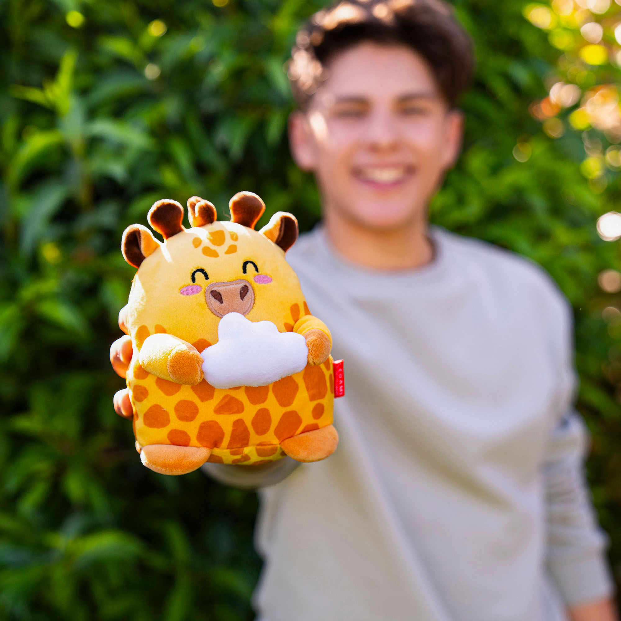 Orangefarbenes Giraffen-Plüschtier, von einer Person vor grünen Pflanzen gehalten gezeigt.