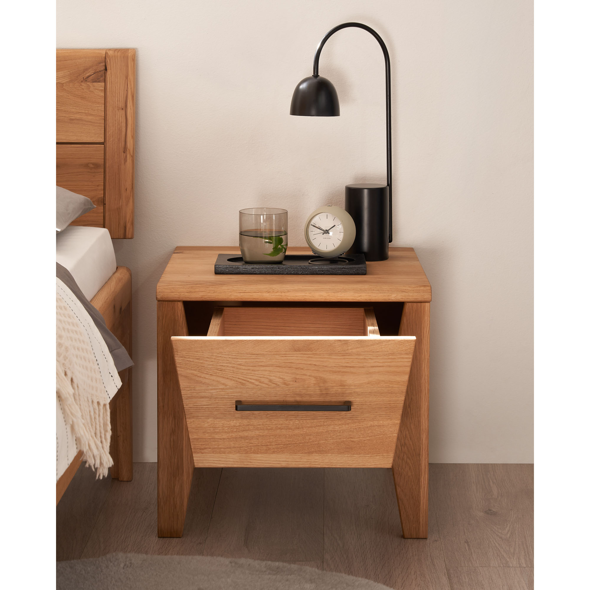 Nachttisch aus Holz mit geöffneter Schublade neben einem Bett im Schlafzimmer