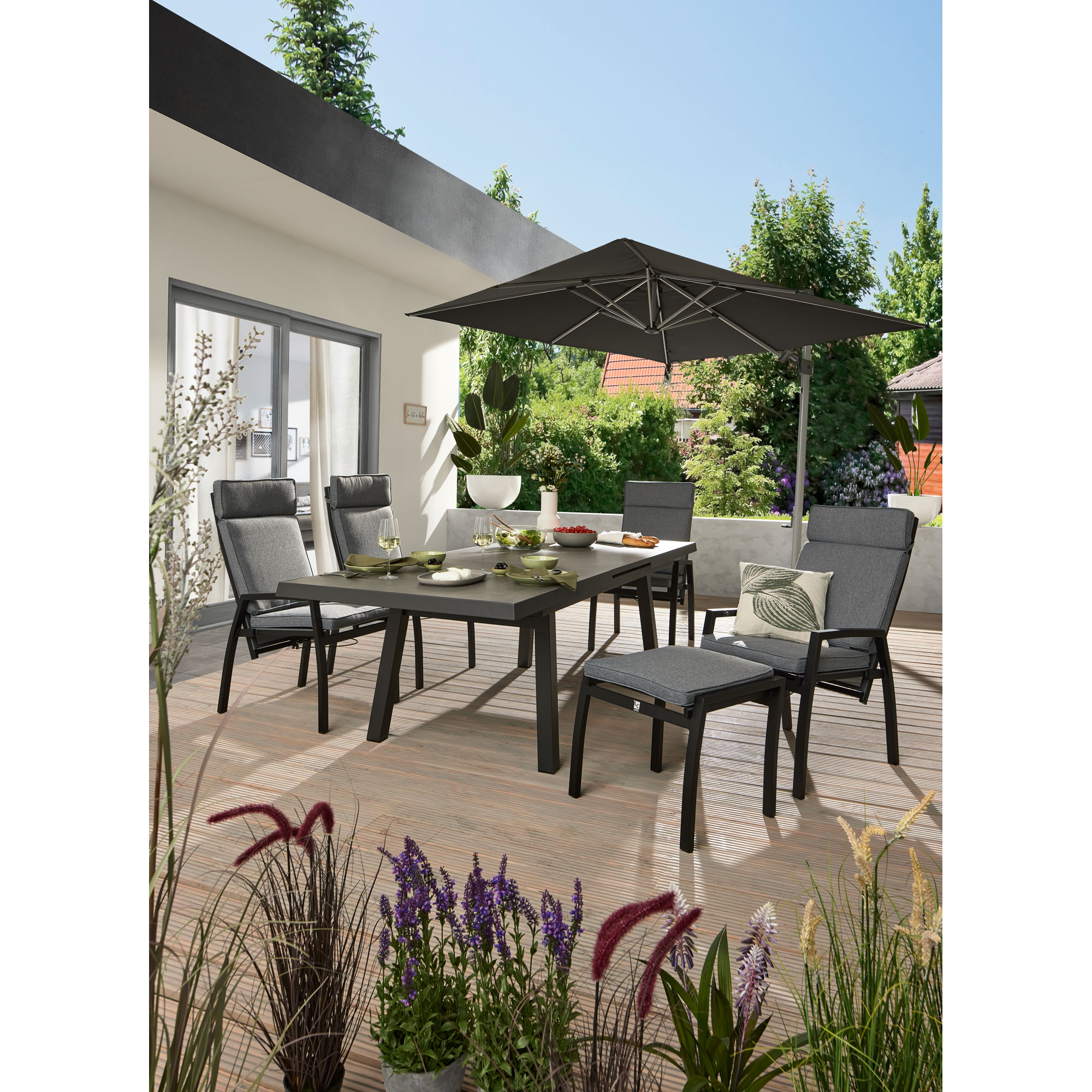 Rechteckiger Gartentisch mit mehreren Gartenstühlen auf einer Terrasse vor einem Wohnhaus