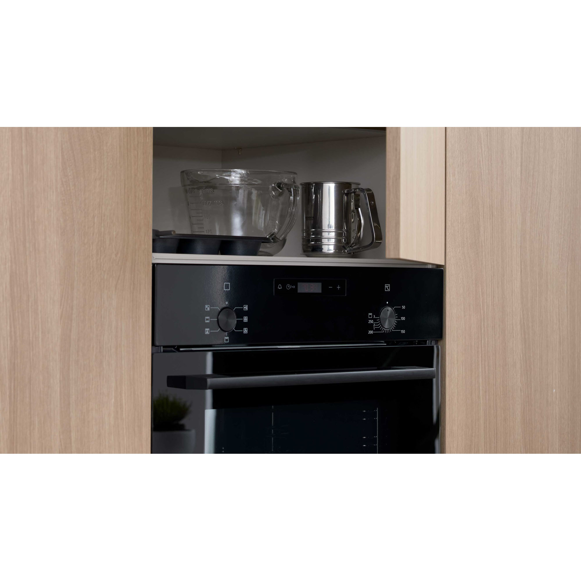 Offenes Stauraumfach über einem Backofen mit Küchenutensilien wie Messbechern und Schüsseln.