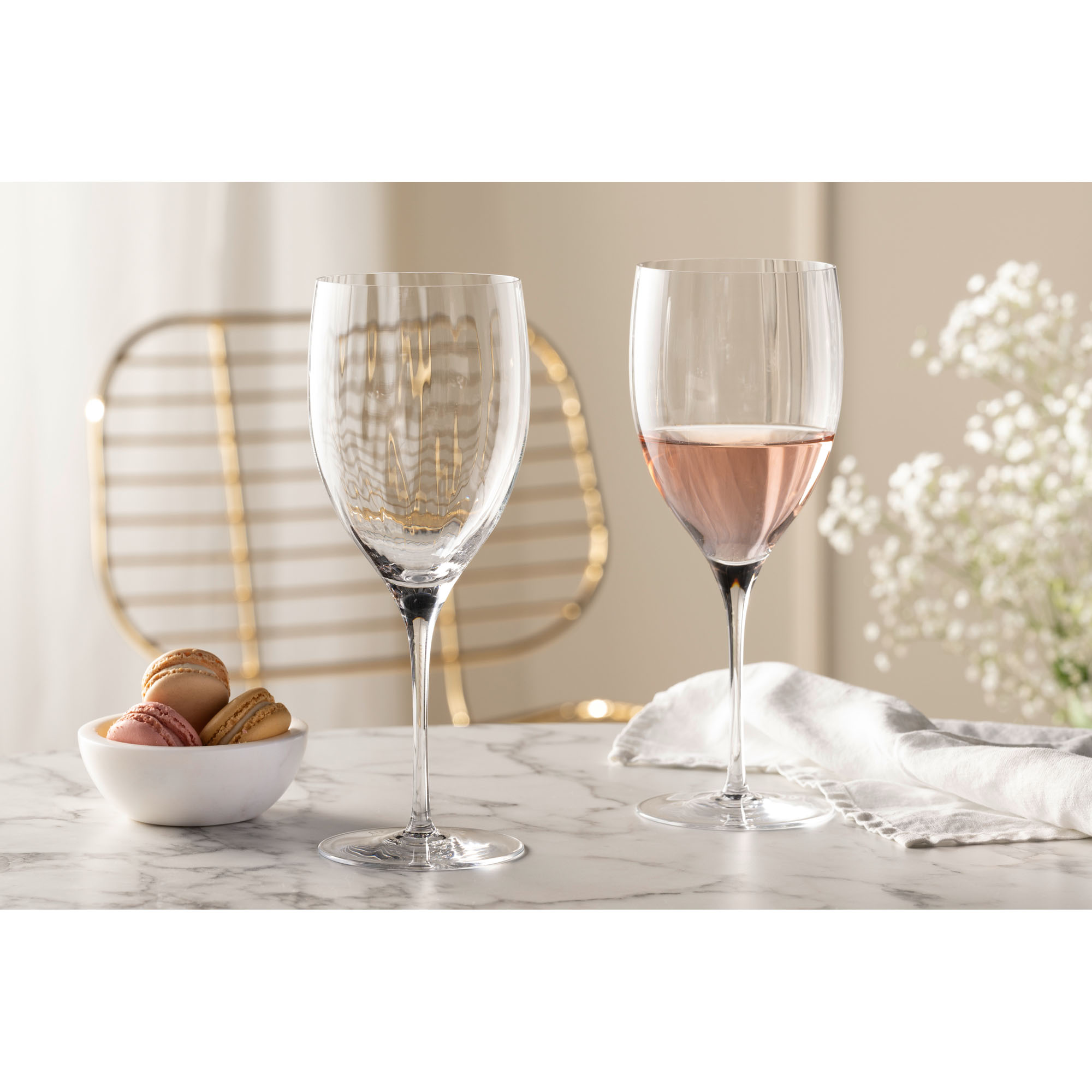 Zwei Weißweingläser eines gefüllt mit Roséwein neben Gebäck und Serviette auf Tisch