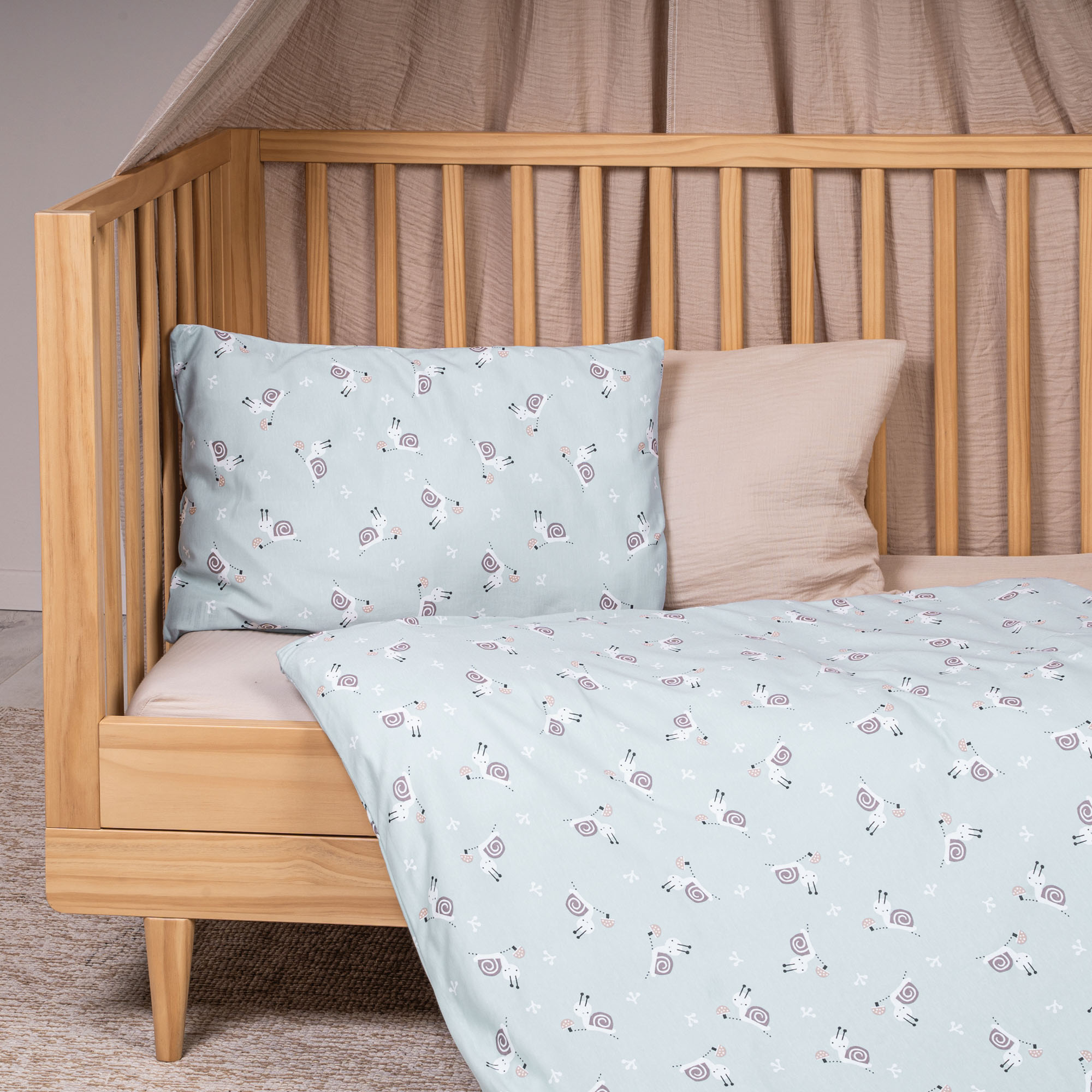 Kinderbett mit Jersey-Bettwäsche in hellem Blau und Schneckenmotiv als Bezug auf Kissen und Decke