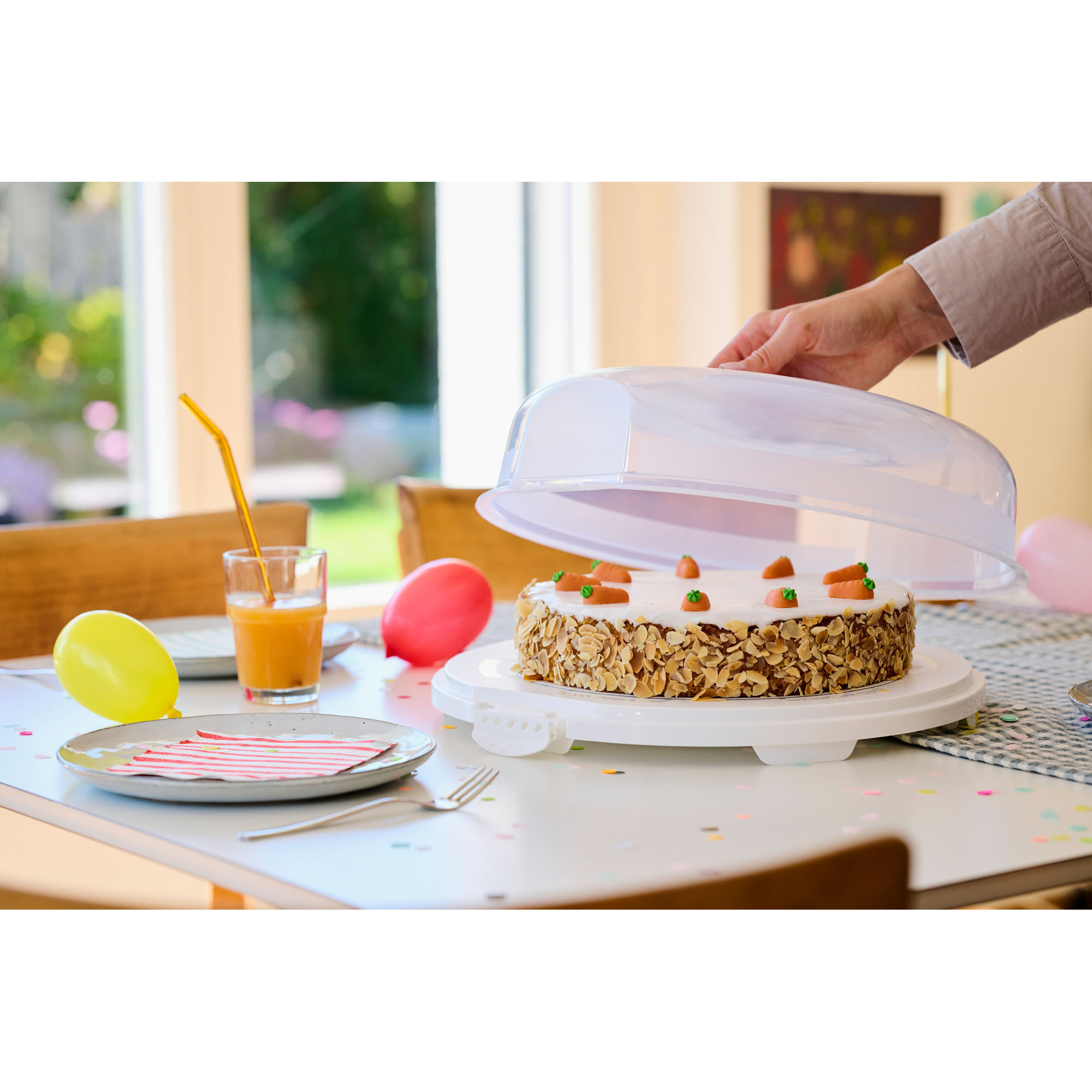 Transparente Kuchenhaube auf einem Unterteller mit Kuchen auf einer Arbeitsfläche