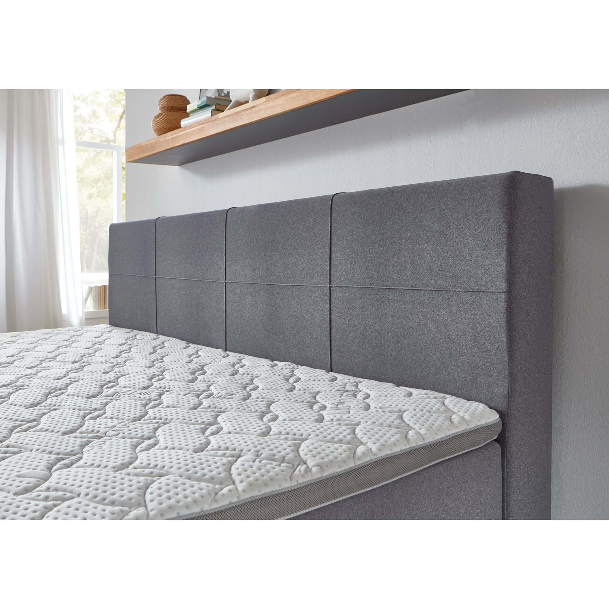 Boxspringbett mit grauem Stoffbezug und gepolstertem Kopfteil mit quadratischer Steppung