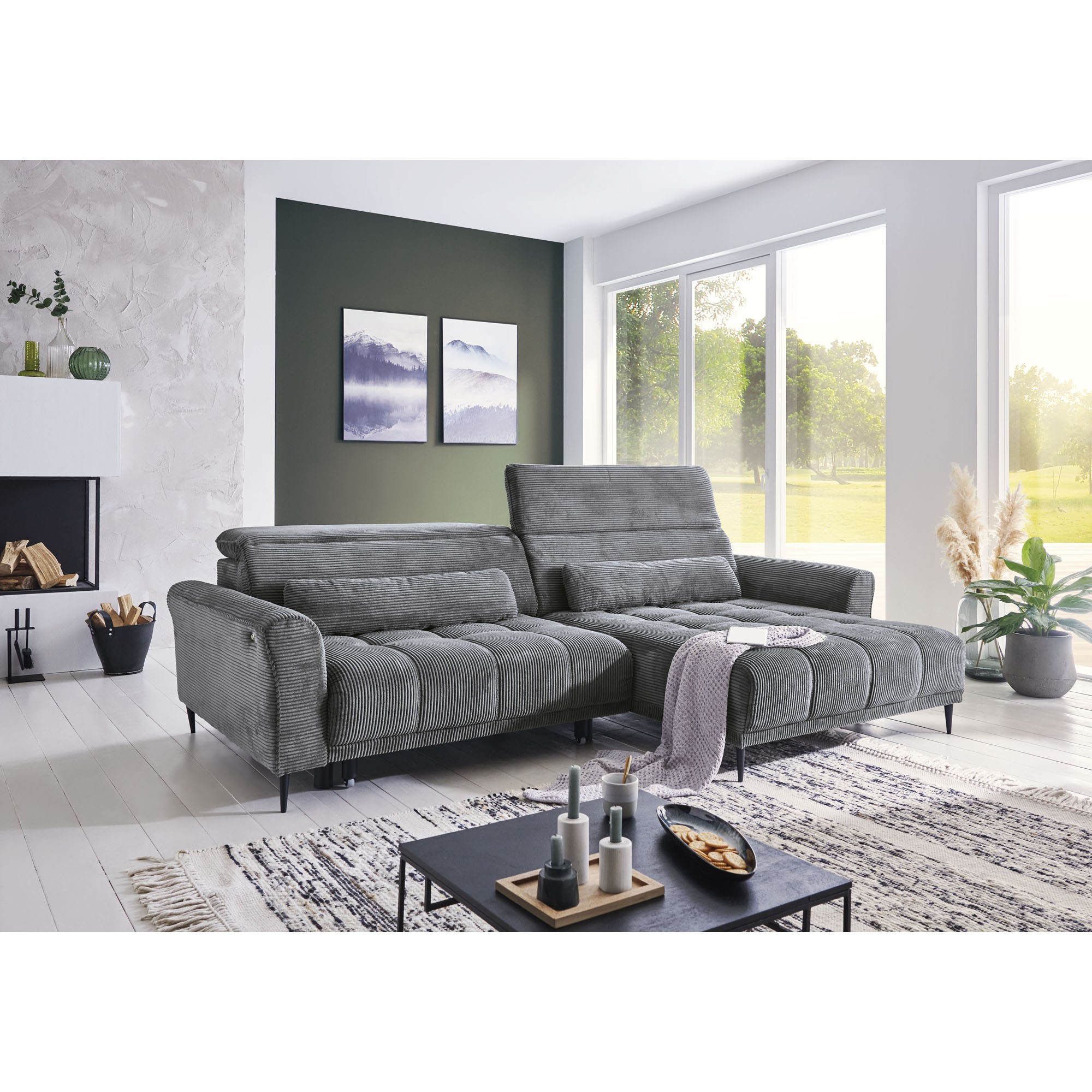Modern eingerichtetes Wohnzimmer mit großem Ecksofa in grauem Cordstoff, helle Atmosphäre mit Blick ins Grüne.